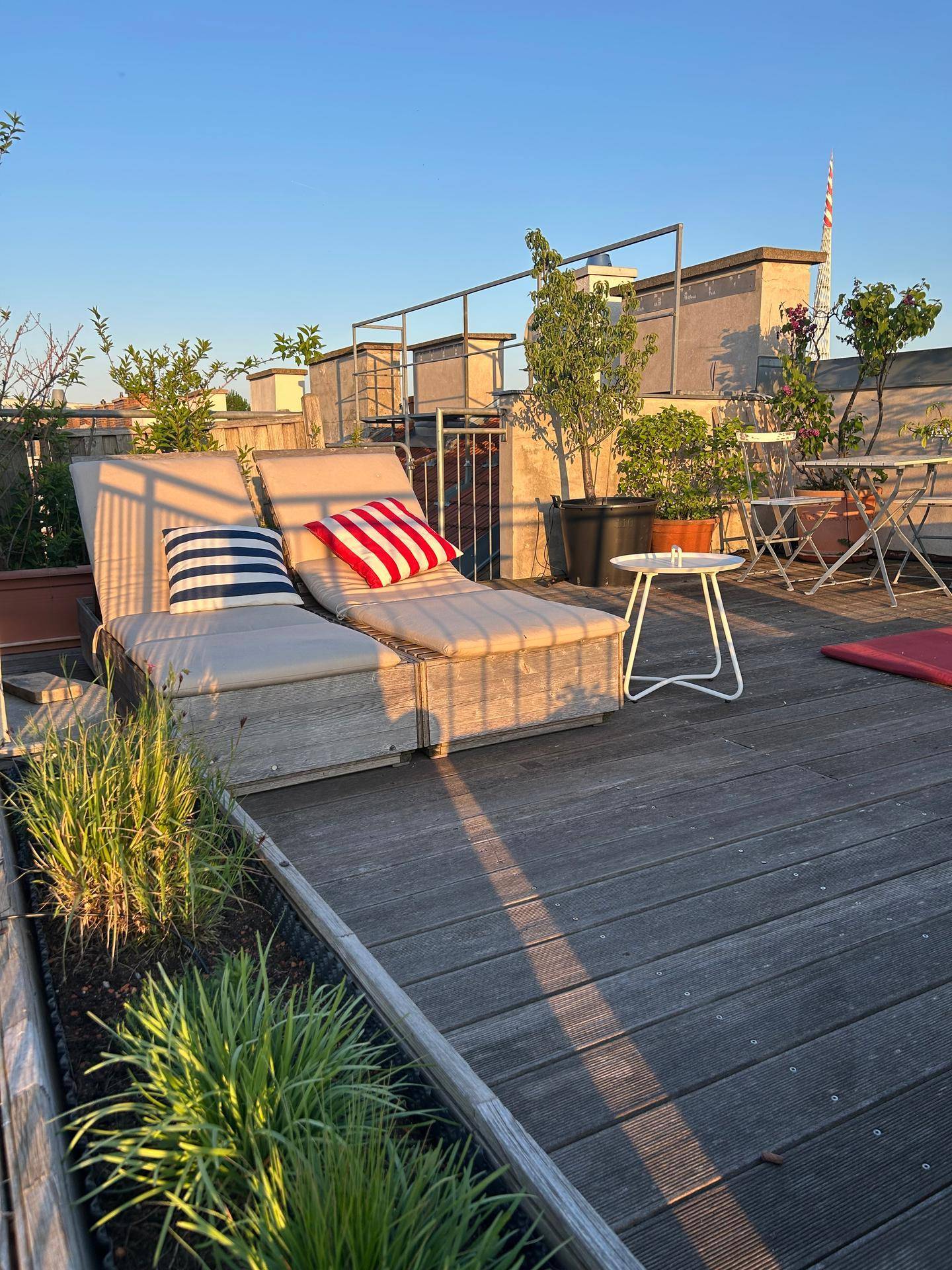 Sonnige Dachterrasse mit Holzdeck, Liegestühlen und Pflanzen, ideal zum Entspannen.