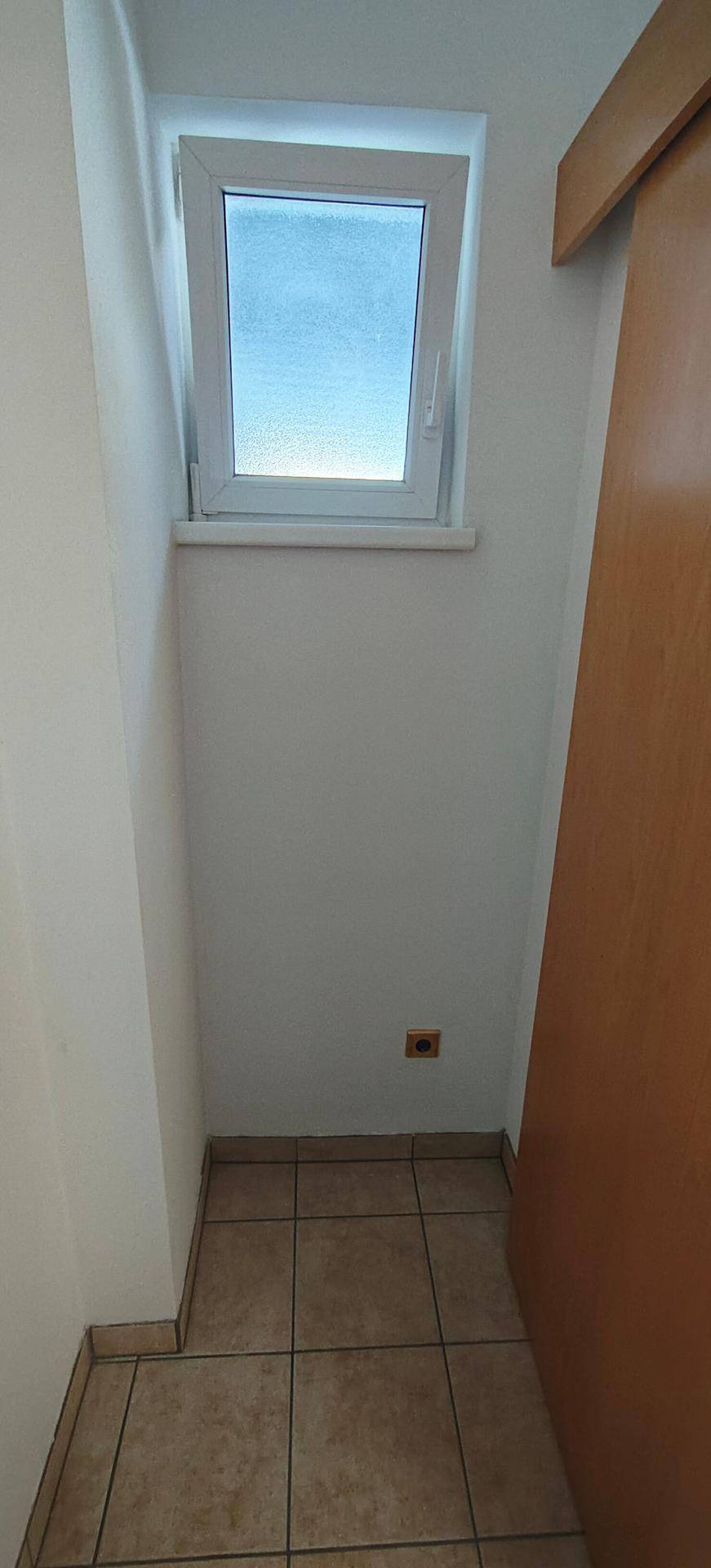 Kleiner Abstellraum mit Fliesenboden und einem Fenster für Tageslicht.