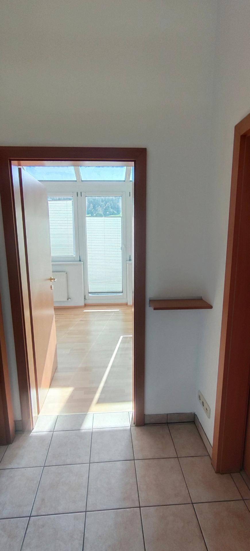 Flur mit Fliesenboden und Blick durch eine offene Tür in einen hellen Raum.