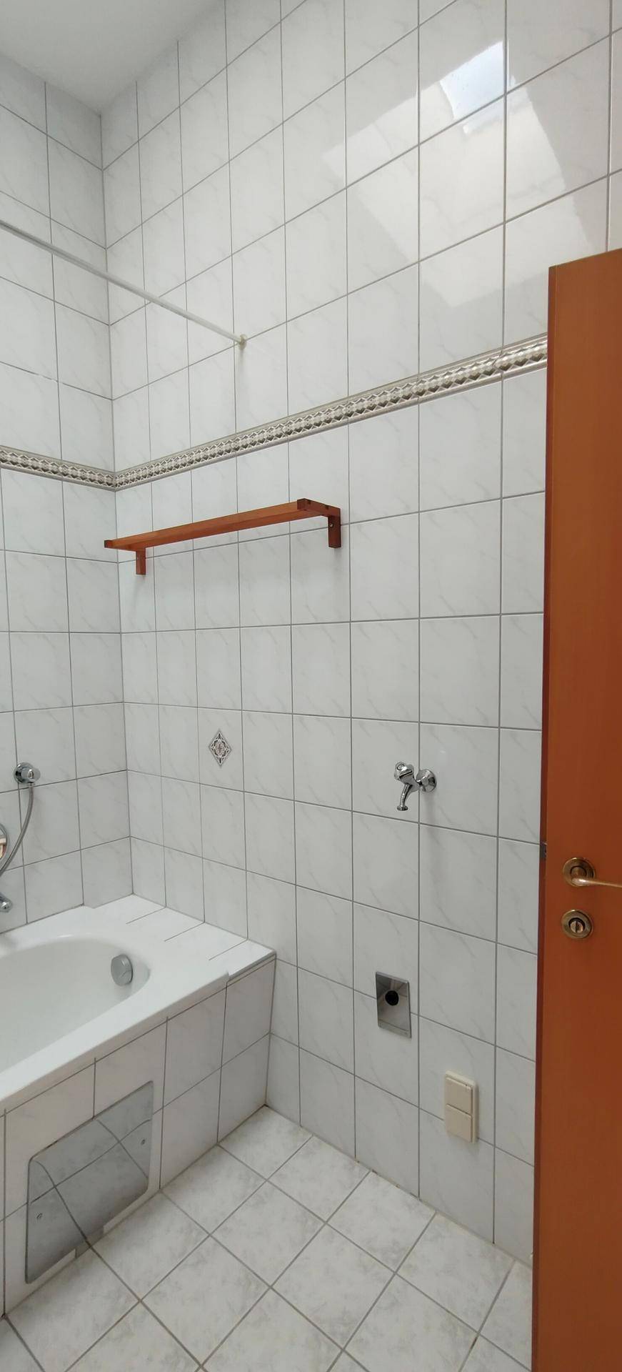 Badezimmer mit Badewanne, Duscharmatur und weißen Fliesen an Wänden und Boden.