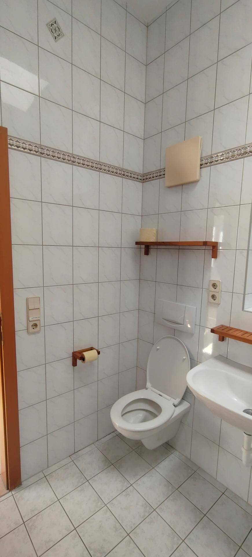 Kleines Badezimmer mit WC, Waschbecken und weißen Wandfliesen.