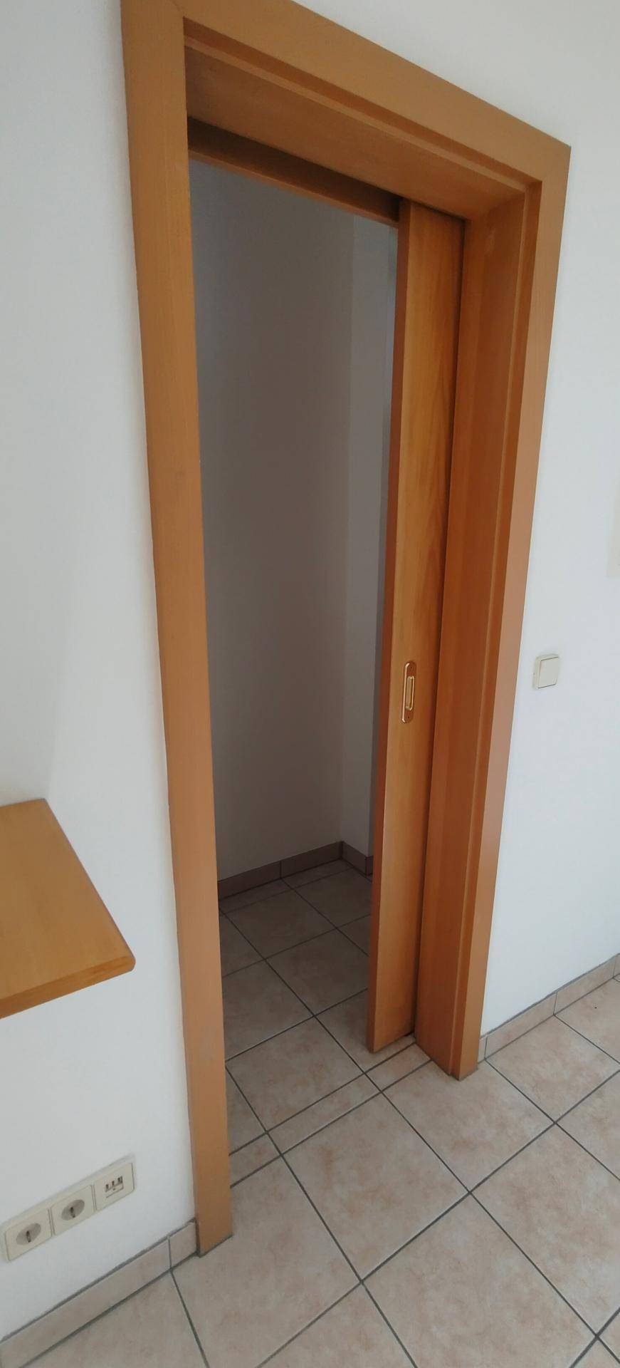 Flur mit Fliesenboden und einer Schiebetür, die zu einem Nebenraum führt.
