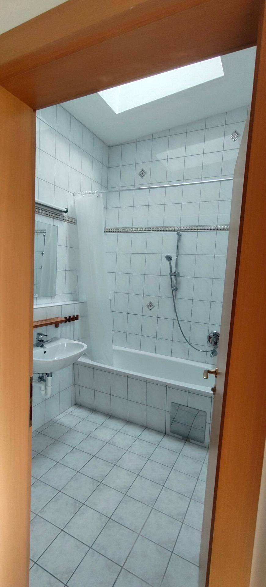 Badezimmer mit Badewanne, Duschvorhang, Waschbecken und hellen Fliesen.