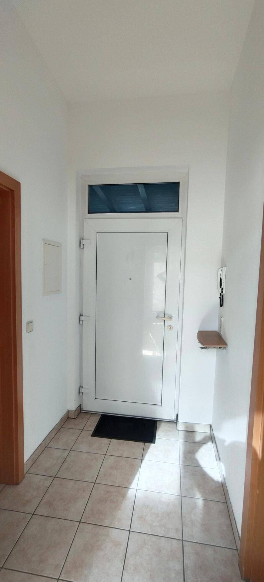 Heller Eingangsbereich mit Fliesenboden und weißer Eingangstür.