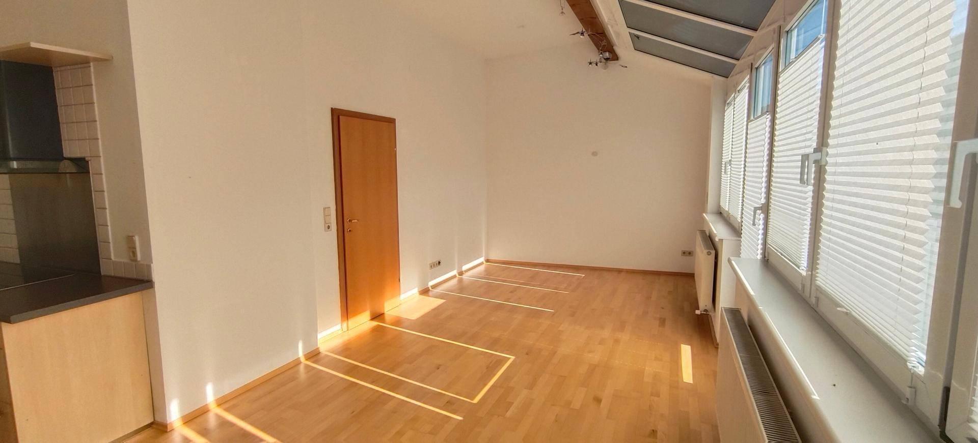 Heller Wohnraum mit Holzboden, großen Fenstern und viel Tageslicht.