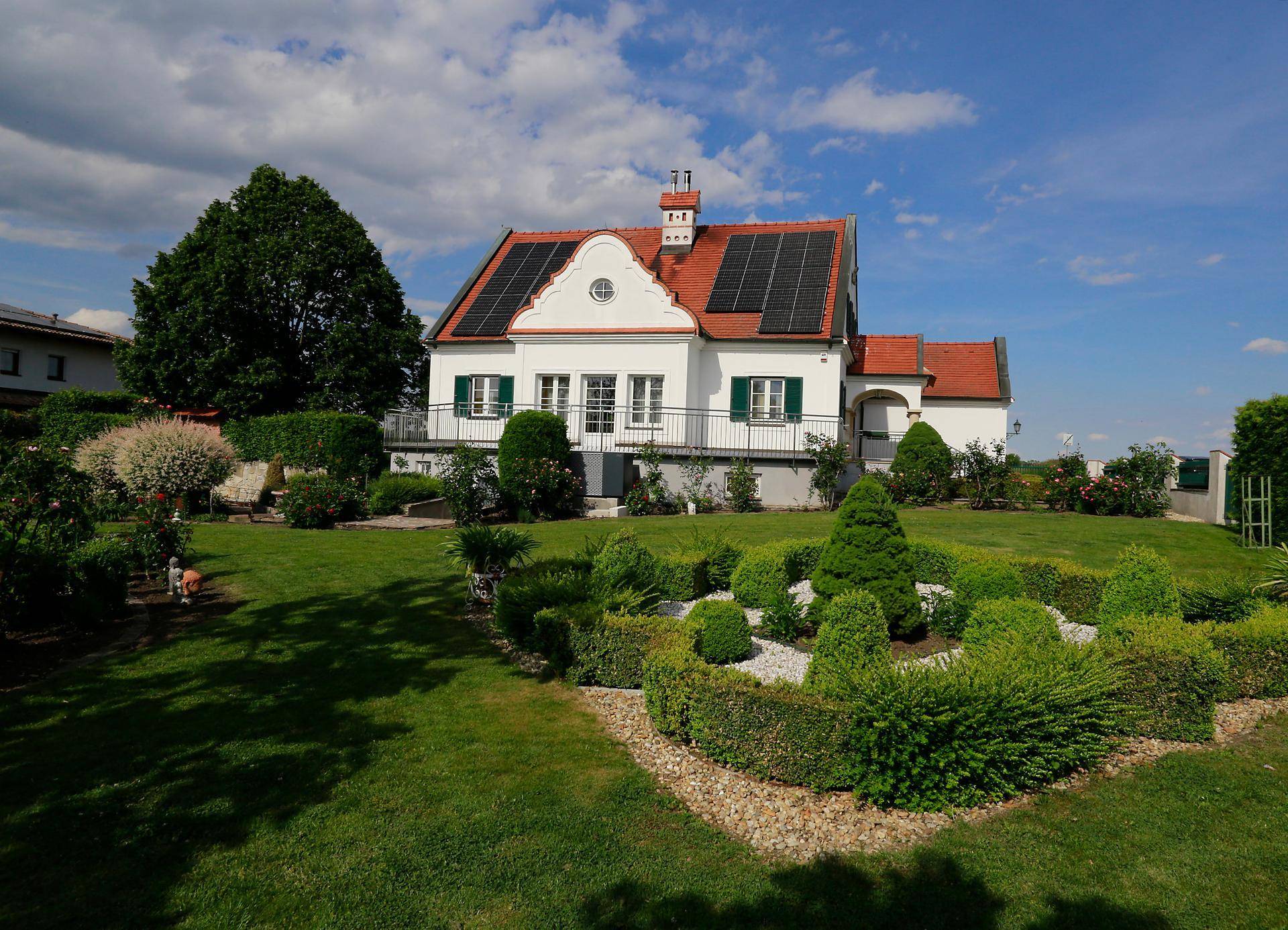 Weitläufiger Garten mit gepflegtem Rasen, dekorativen Hecken und dem Haus mit Solaranlage im Hintergrund.