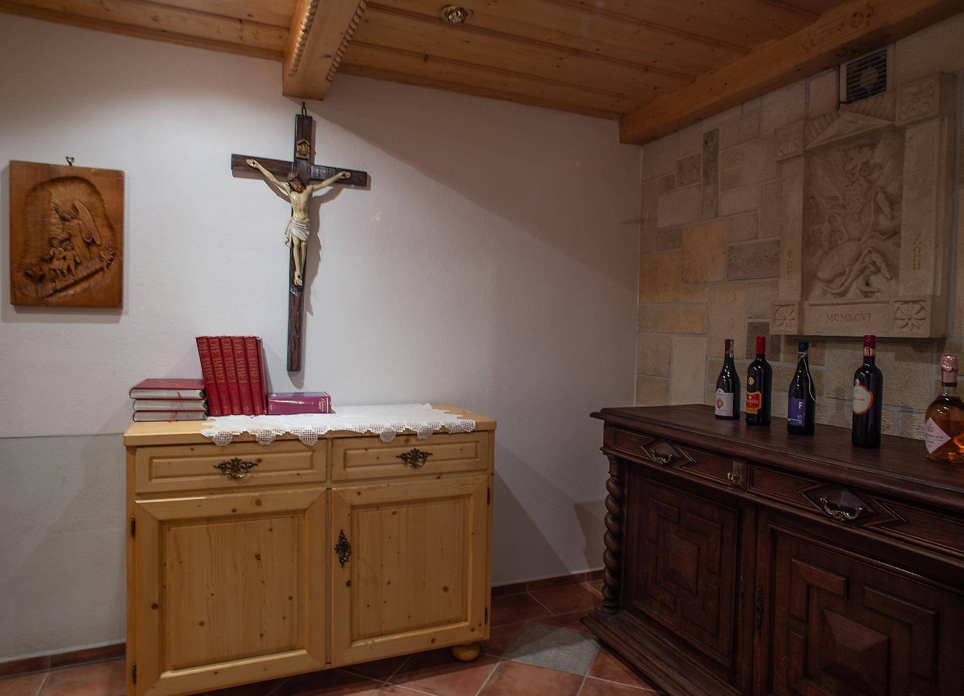 Rustikaler Raum mit Holzbalkendecke, Fliesenboden und einem Holzschrank, dekoriert mit religiösen Gegenständen.