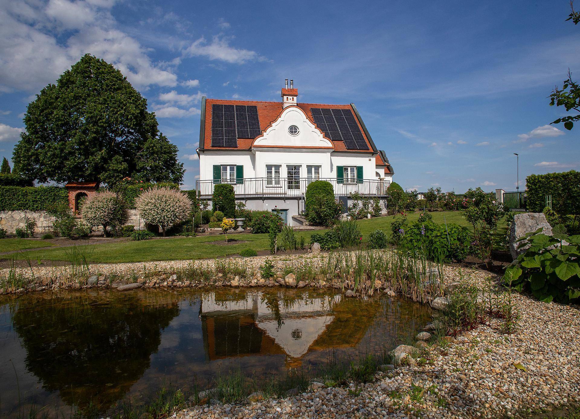 Malerischer Garten mit einem Teich, der das Haus spiegelt, umgeben von Kieswegen und vielfältigen Pflanzen.
