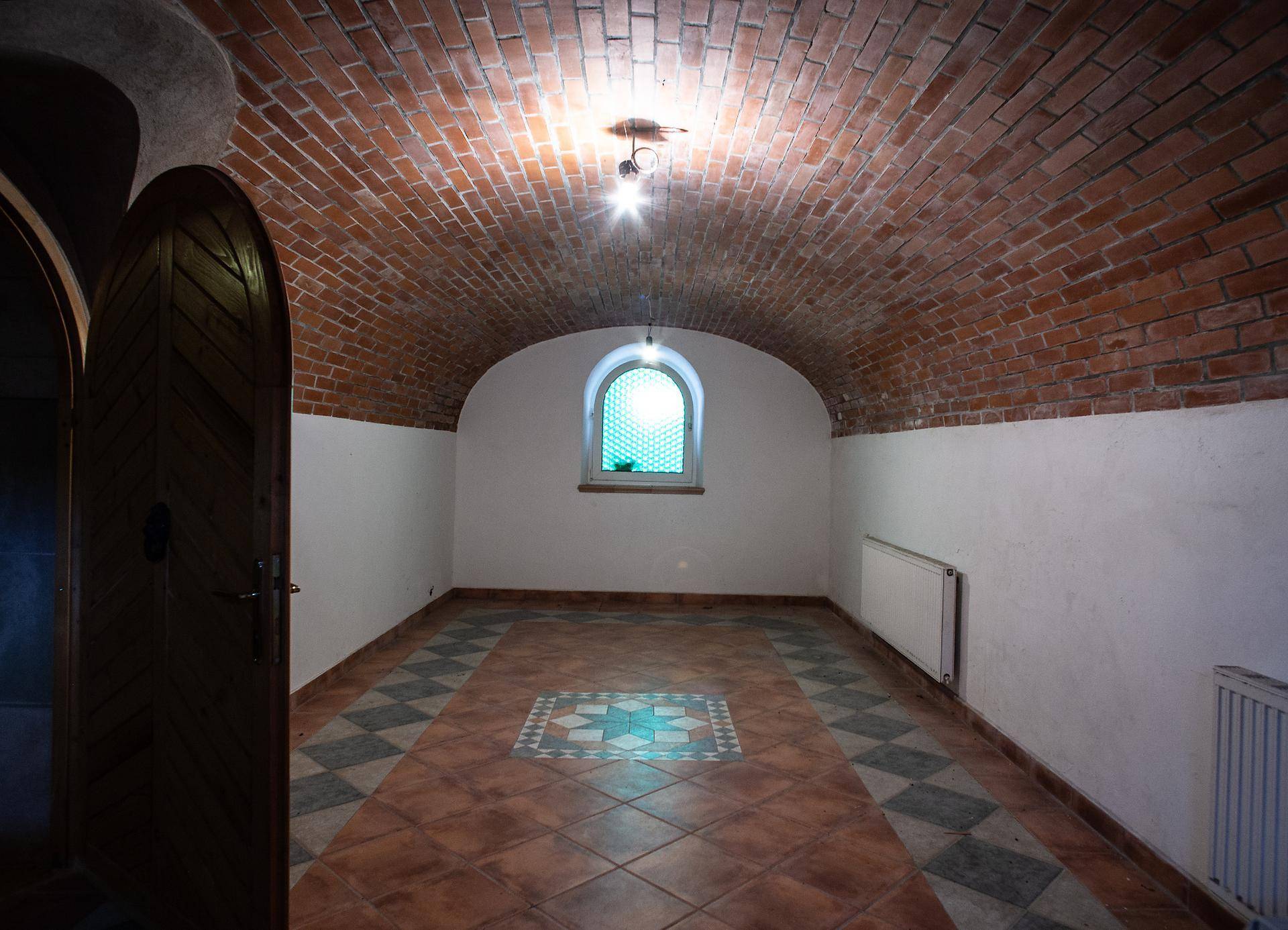 Gewölbter Kellerraum mit Ziegeldecke, gemustertem Fliesenboden und einem kleinen, bogenförmigen Fenster.
