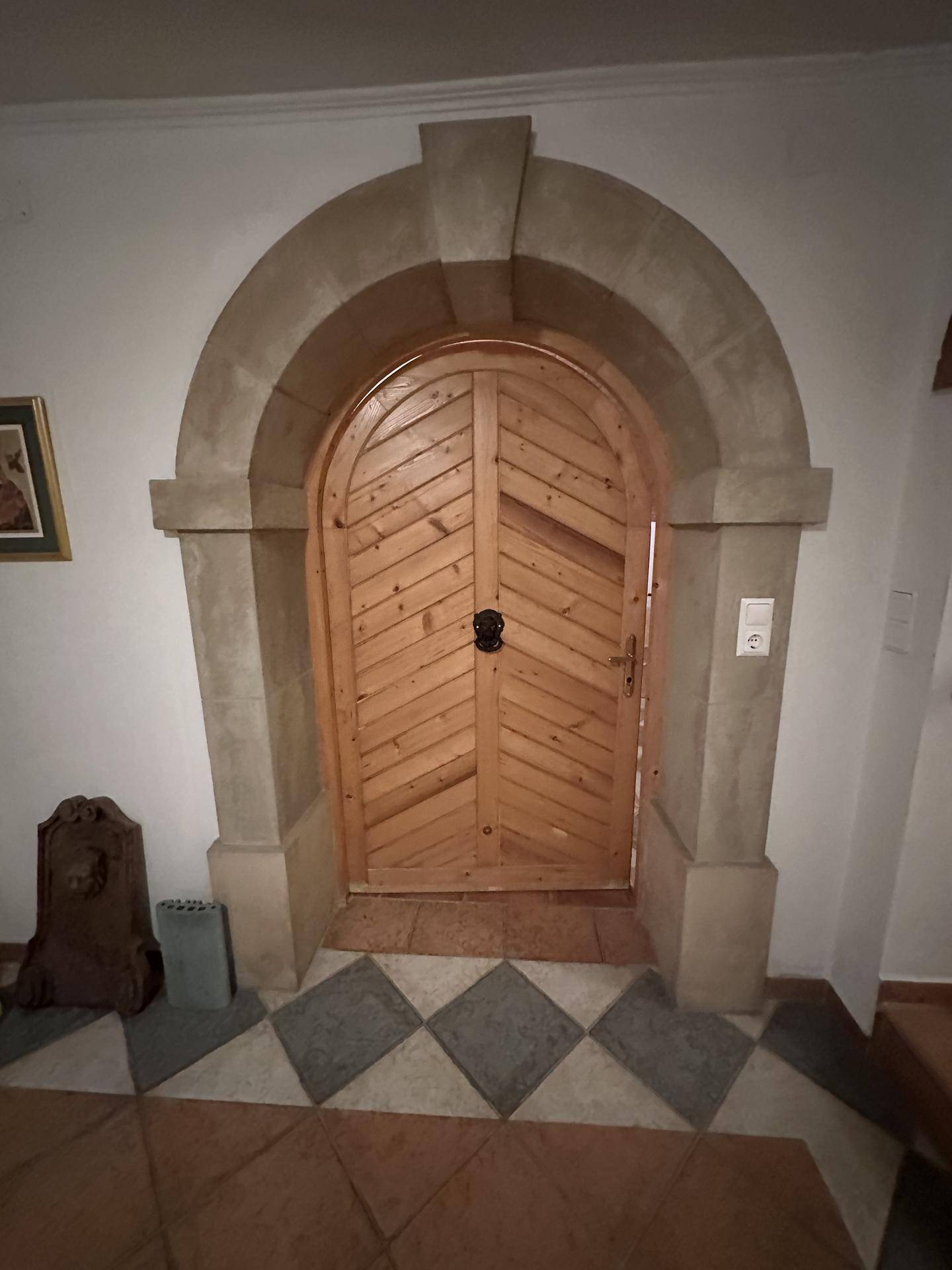 Rustikale Holztür in einem steinernen Bogenrahmen mit gemustertem Fliesenboden im Eingangsbereich.