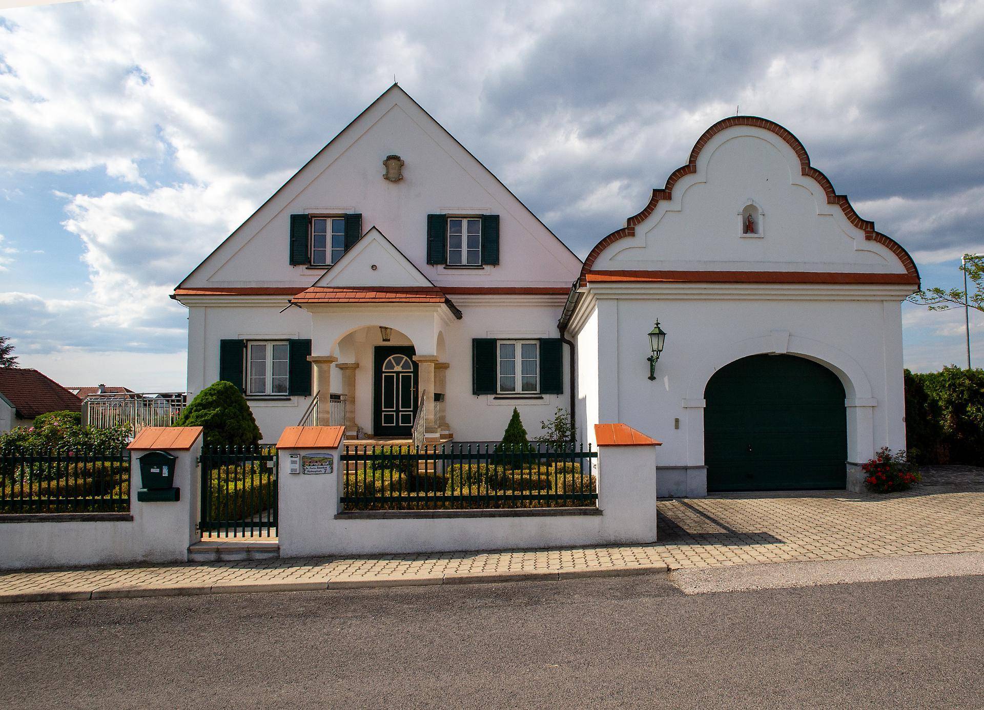 Vorderansicht des Hauses mit Haupteingang und einer angrenzenden Garage mit großem, dunklem Tor.