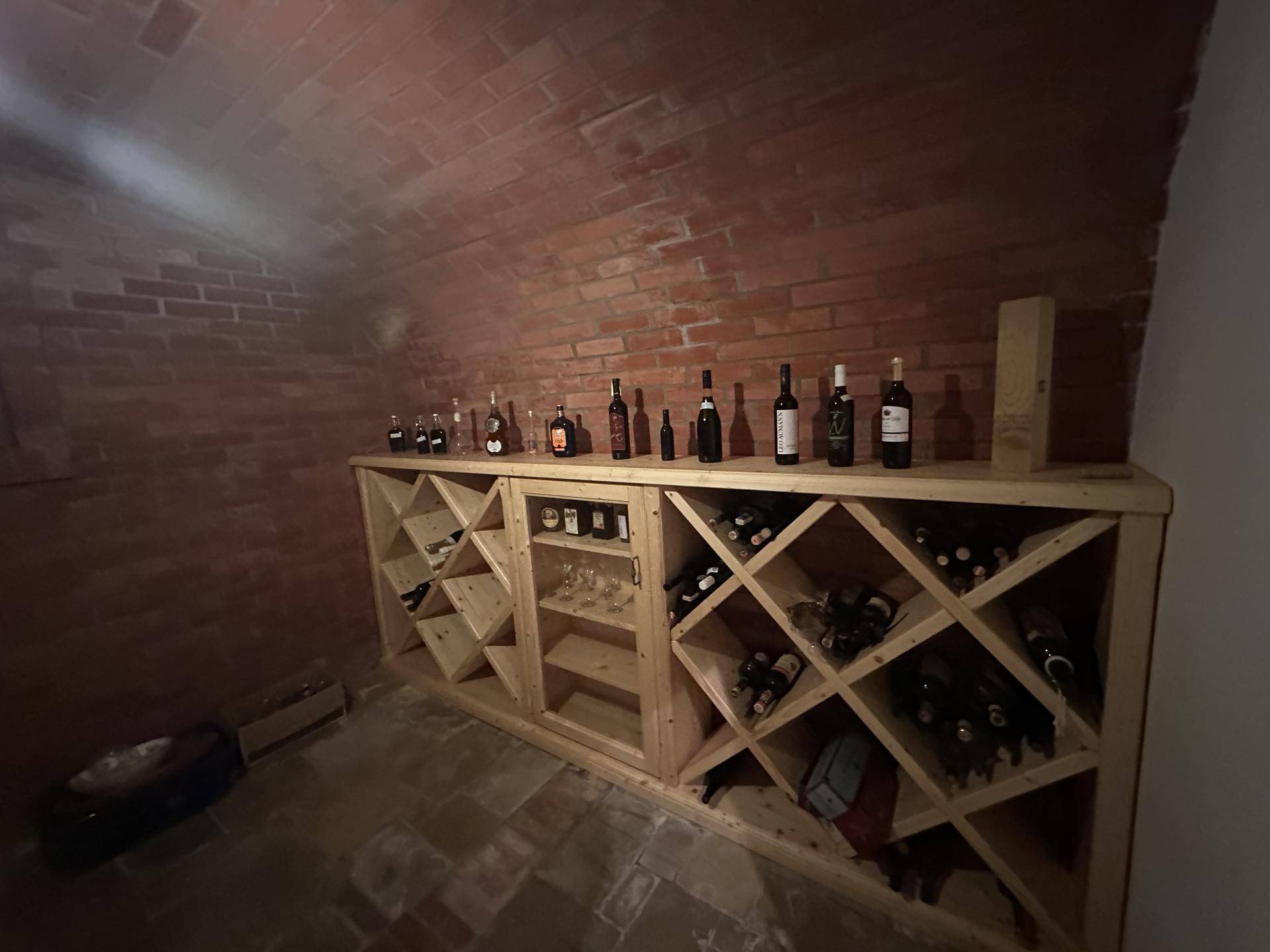 Nahaufnahme der Holzweinregale im Keller, gefüllt mit Flaschen unter der Ziegelgewölbedecke.