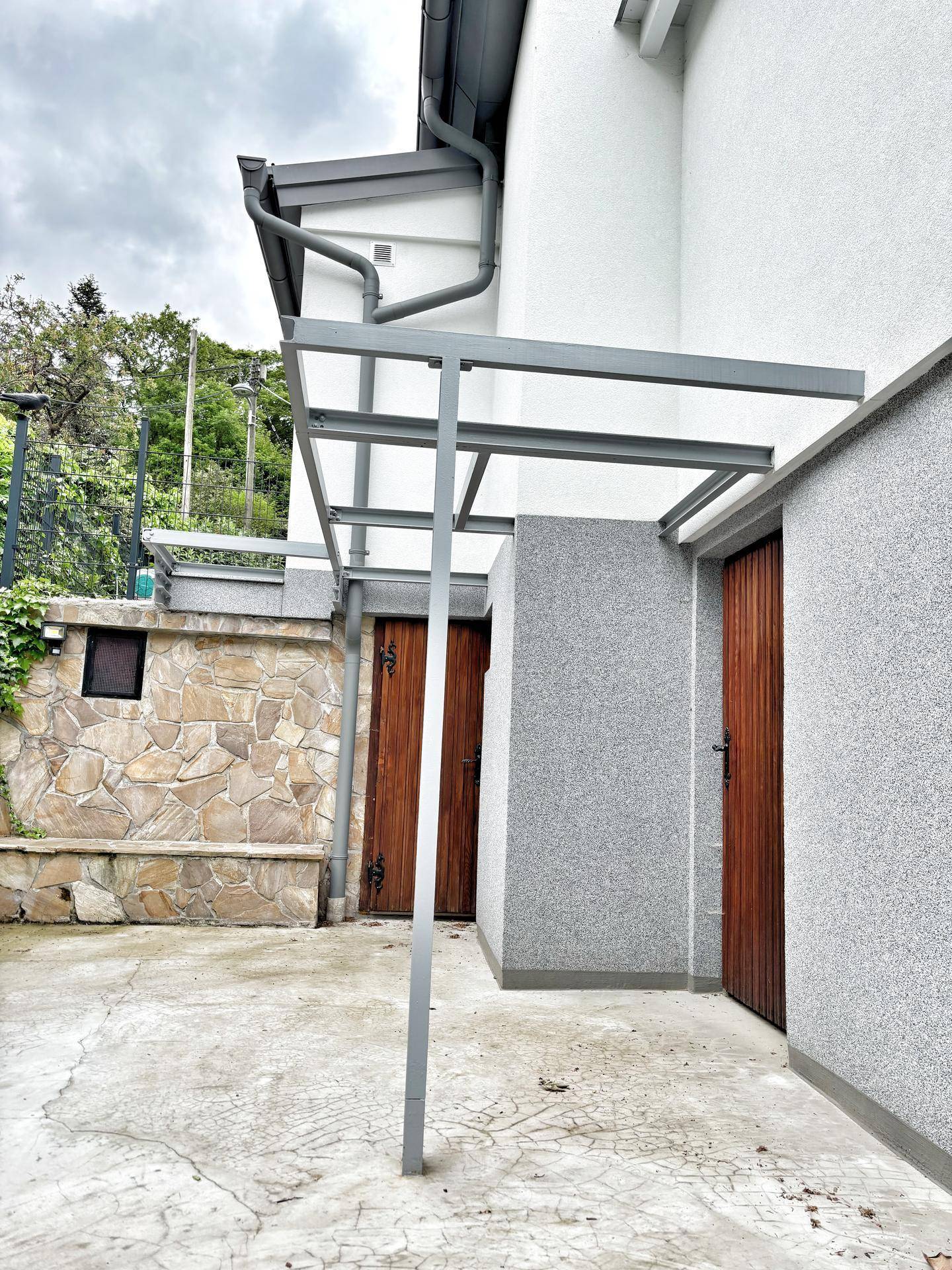 Überdachter Eingangsbereich mit zwei Holztüren und einer modernen Metallkonstruktion.