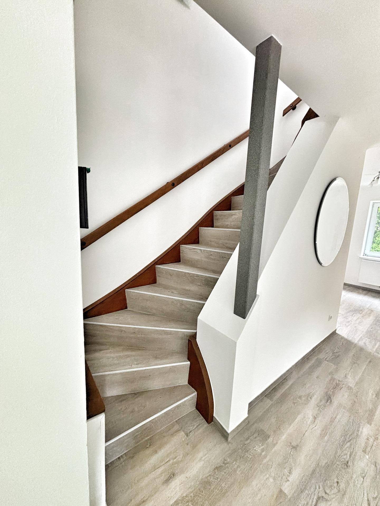 Moderne Holztreppe mit hellem Laminat und weiß gestrichenen Wänden, die nach oben führt.