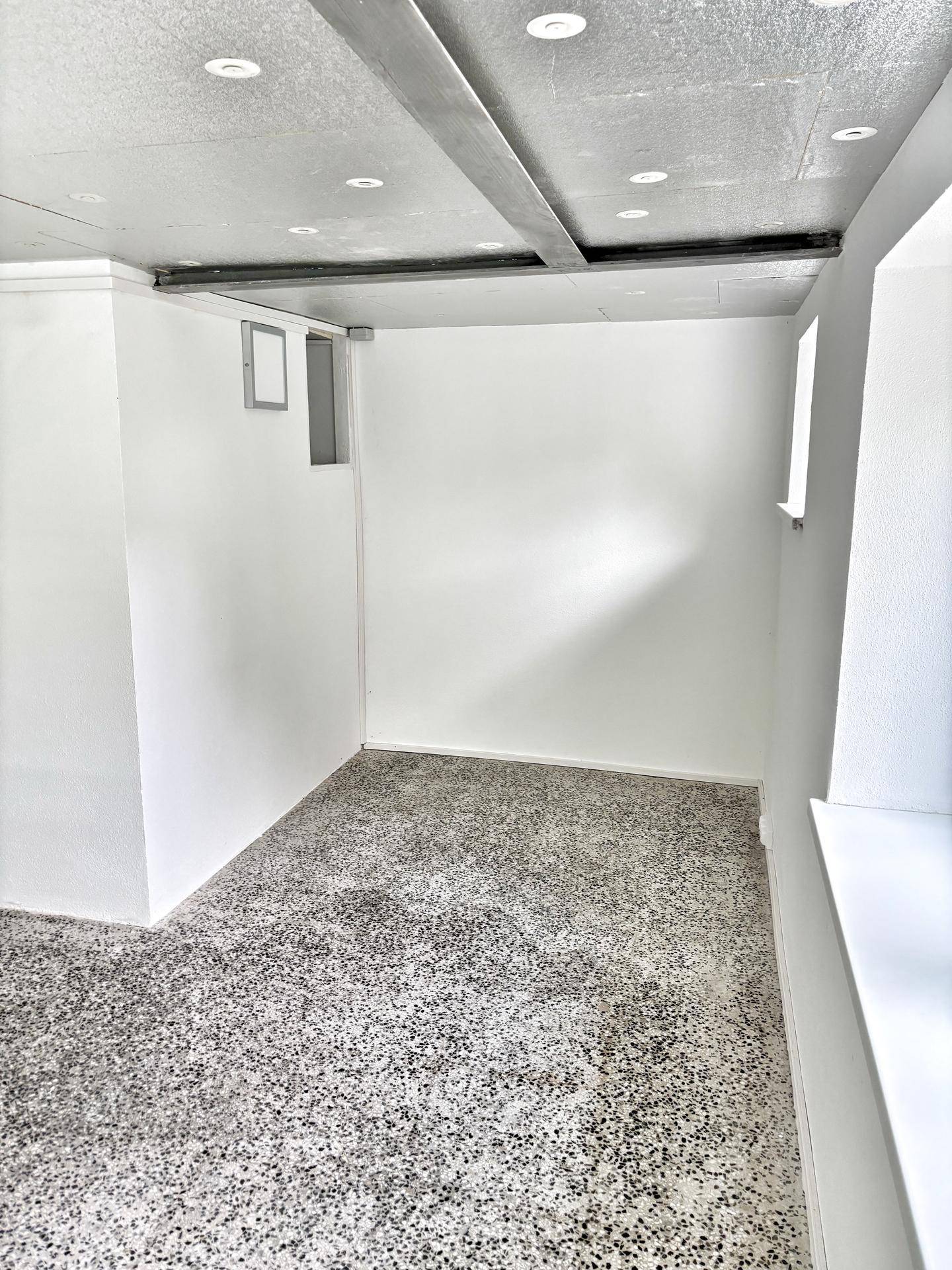 Leerer Raum im Untergeschoss mit Terrazzoboden und einem kleinen Fenster, vielseitig nutzbar.