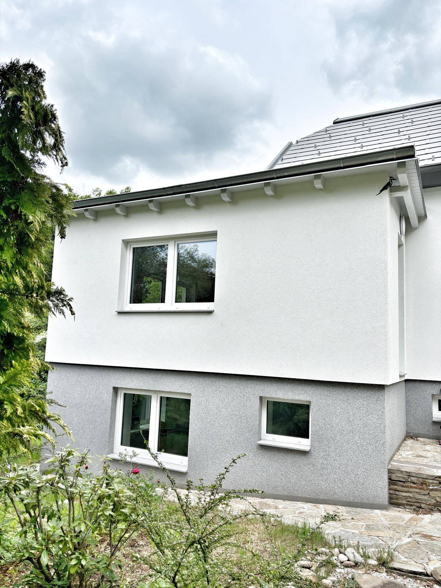 Seitenansicht des Hauses mit weißer Fassade, grauer Sockelzone und Fenstern.