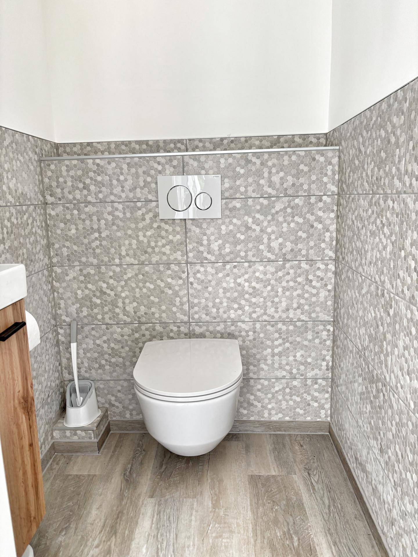 Modernes Gäste-WC mit Wand-WC, grauen sechseckigen Fliesen und hellem Laminatboden.