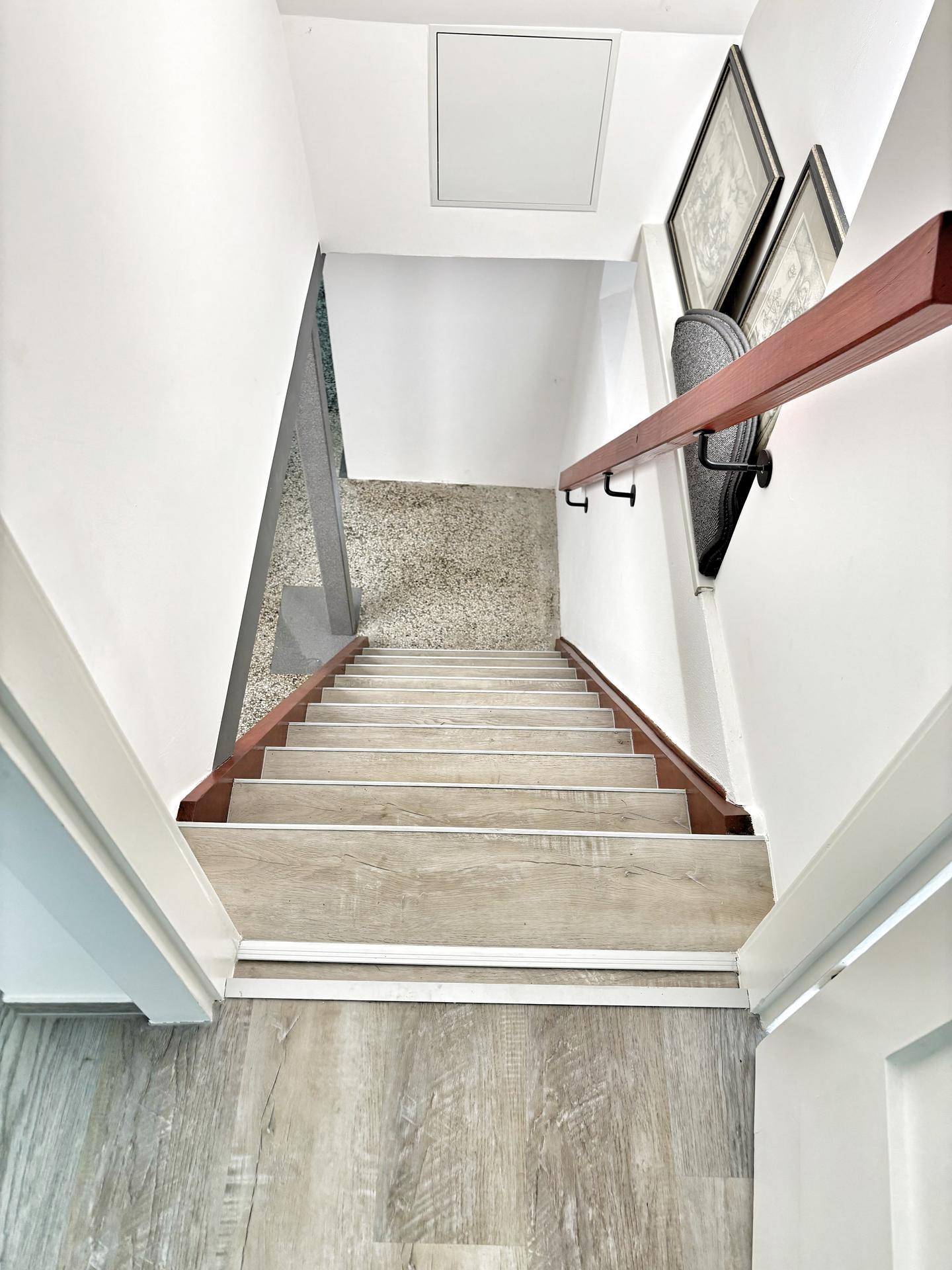 Treppenhaus mit hellen Holzstufen und dunklem Handlauf, das zu einem Raum mit Terrazzoboden führt.