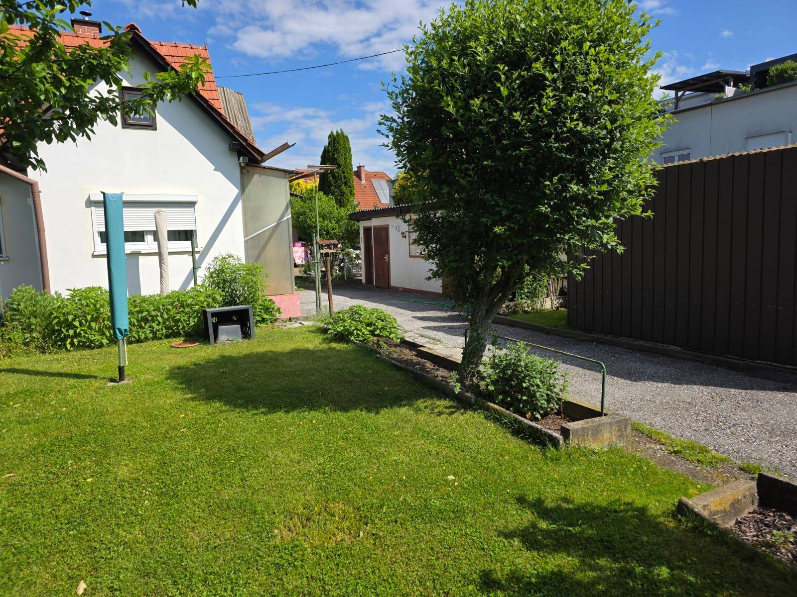 Blick auf das Haus mit Gartenbereich, Zufahrt und einem kleinen Schuppen im Hintergrund.