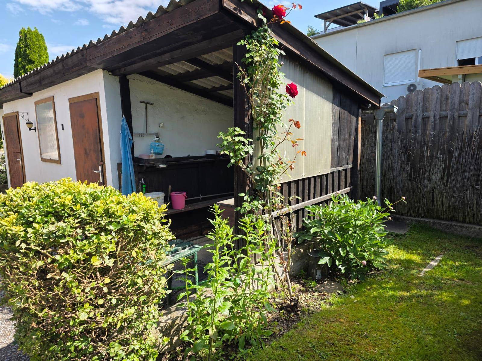 Rustikaler Gartenschuppen mit überdachtem Bereich und Kletterpflanzen an der Holzfassade.
