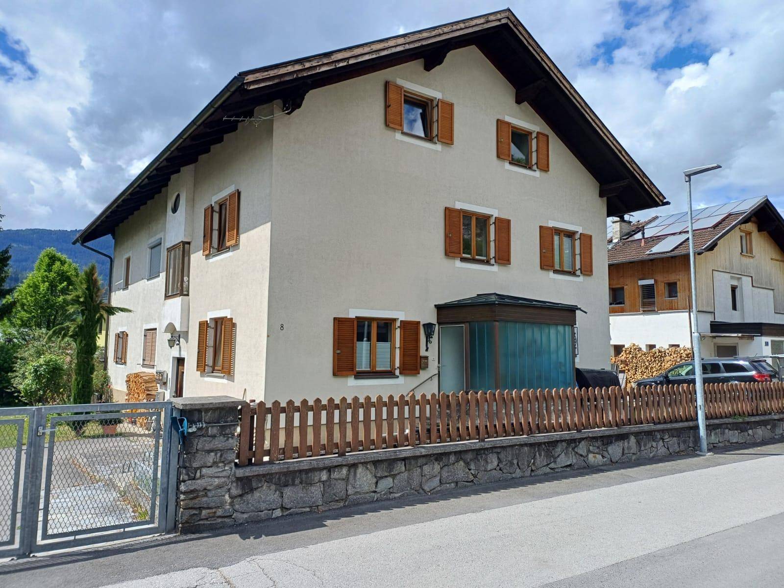 Traditionelles Haus mit heller Fassade, braunen Holzfensterläden und Holzzaun.