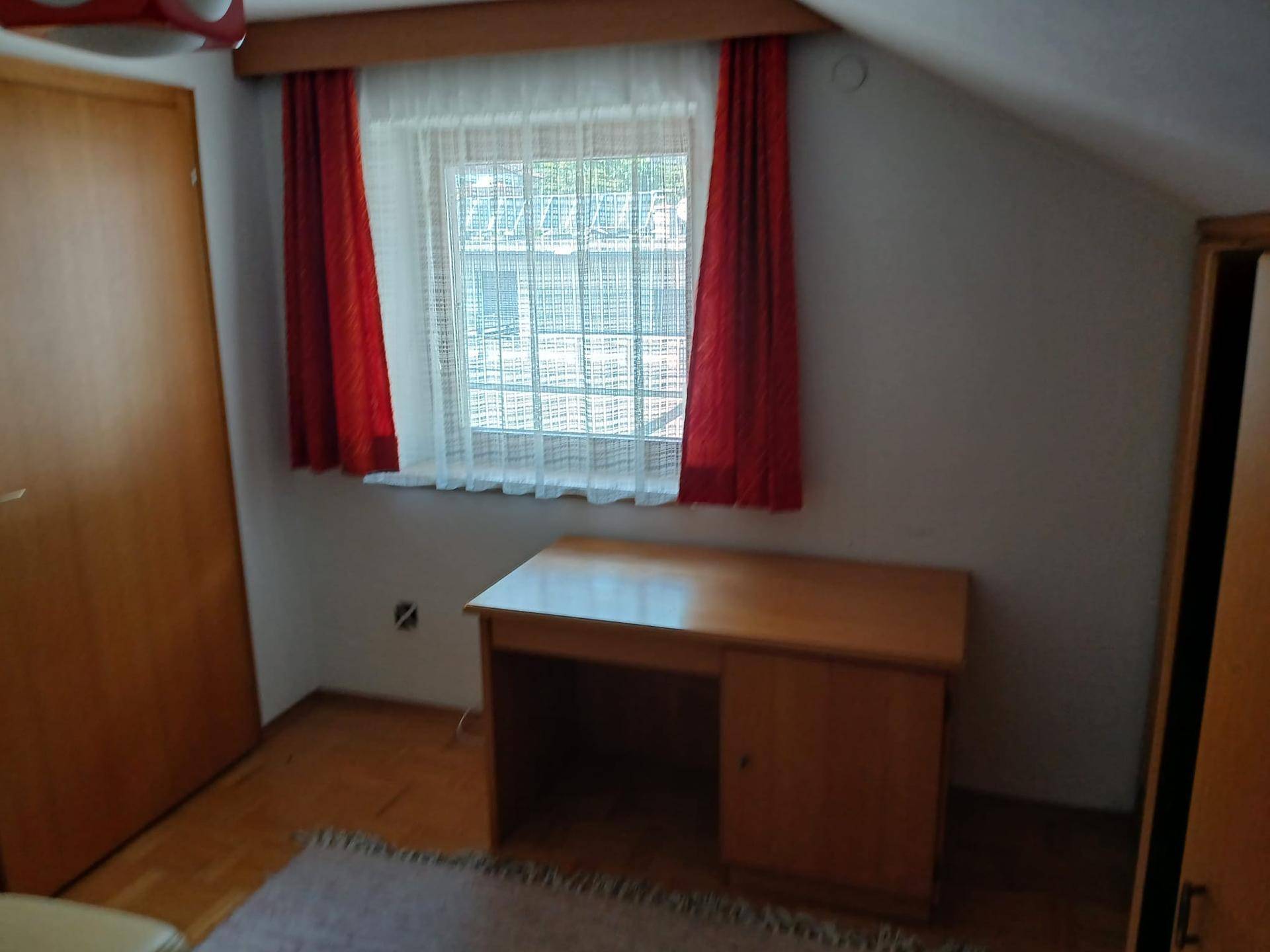 Schlafzimmer im Dachgeschoss mit Schreibtisch, Fenster und roten Vorhängen.