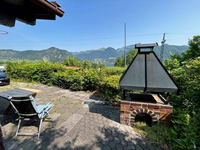 Gepflasterte Terrasse mit gemauertem Grill und weitem Blick auf See und Berge.