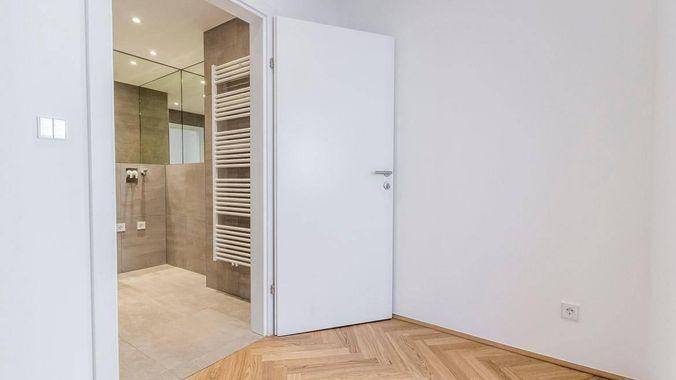 Offene Tür zu einem Badezimmer, daneben ein Raum mit Fischgrätparkett.