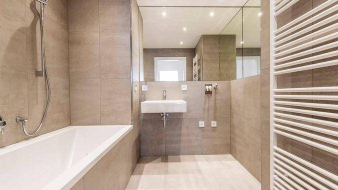 Modernes Badezimmer mit Badewanne, großem Spiegel und beigefarbenen Fliesen.