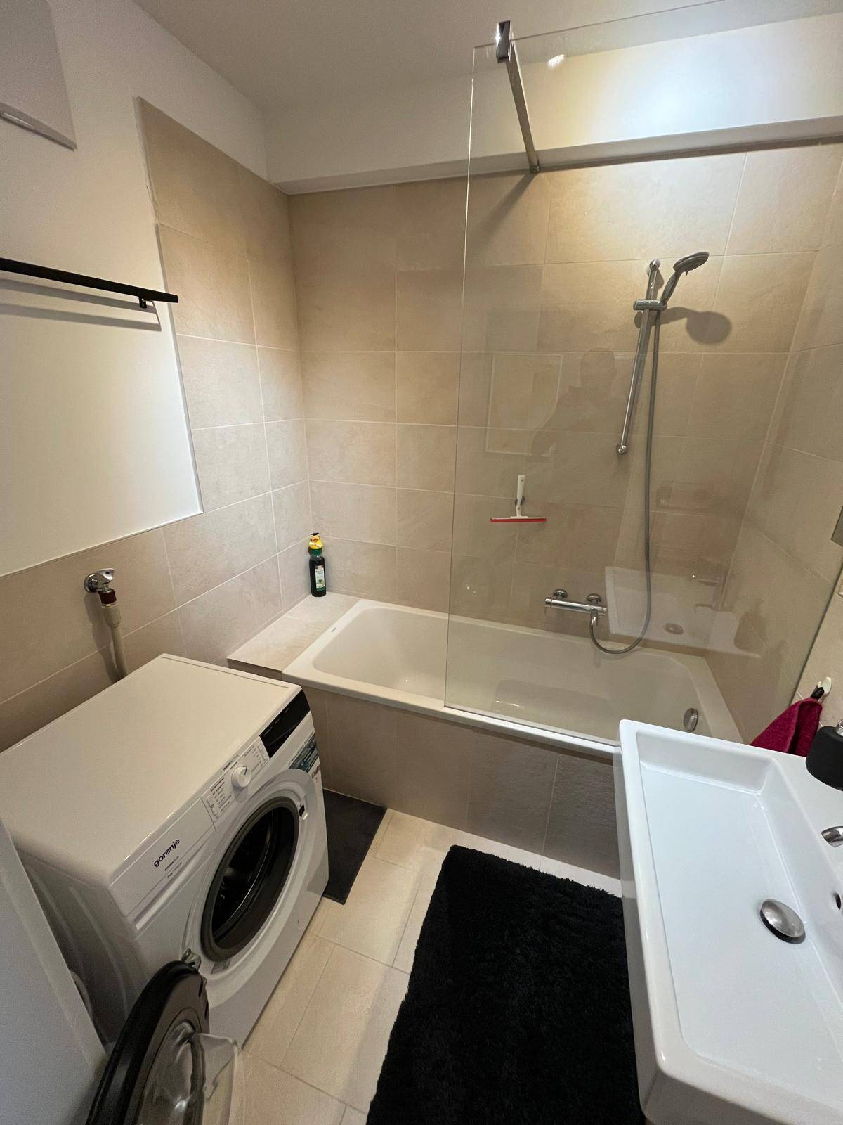Modernes Badezimmer mit Badewanne, Dusche, Waschbecken und Waschmaschine, hell gefliest.