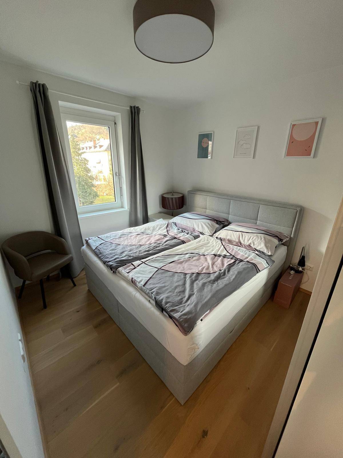 Helles Schlafzimmer mit Doppelbett, Holzboden und einem Fenster mit Blick ins Grüne.