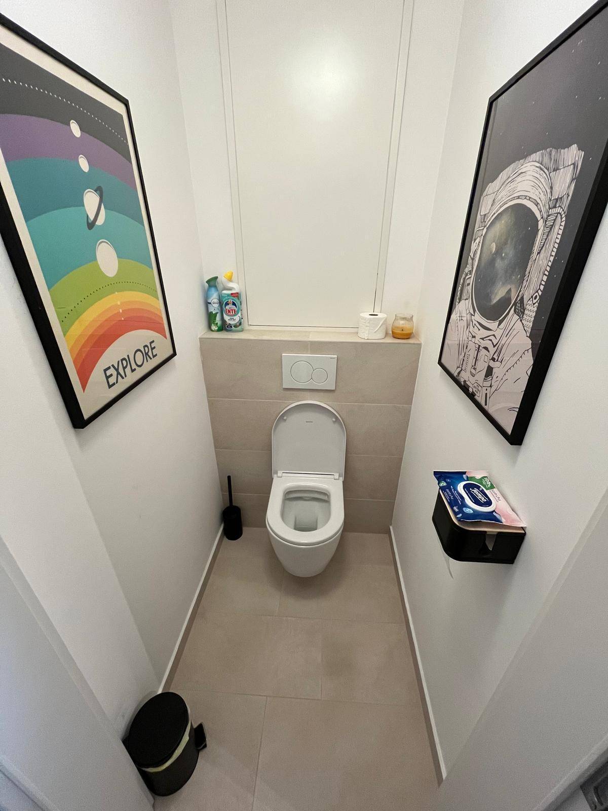 Separates WC mit Wand-WC und modernen Bildern an den Wänden, in schlichtem Design.