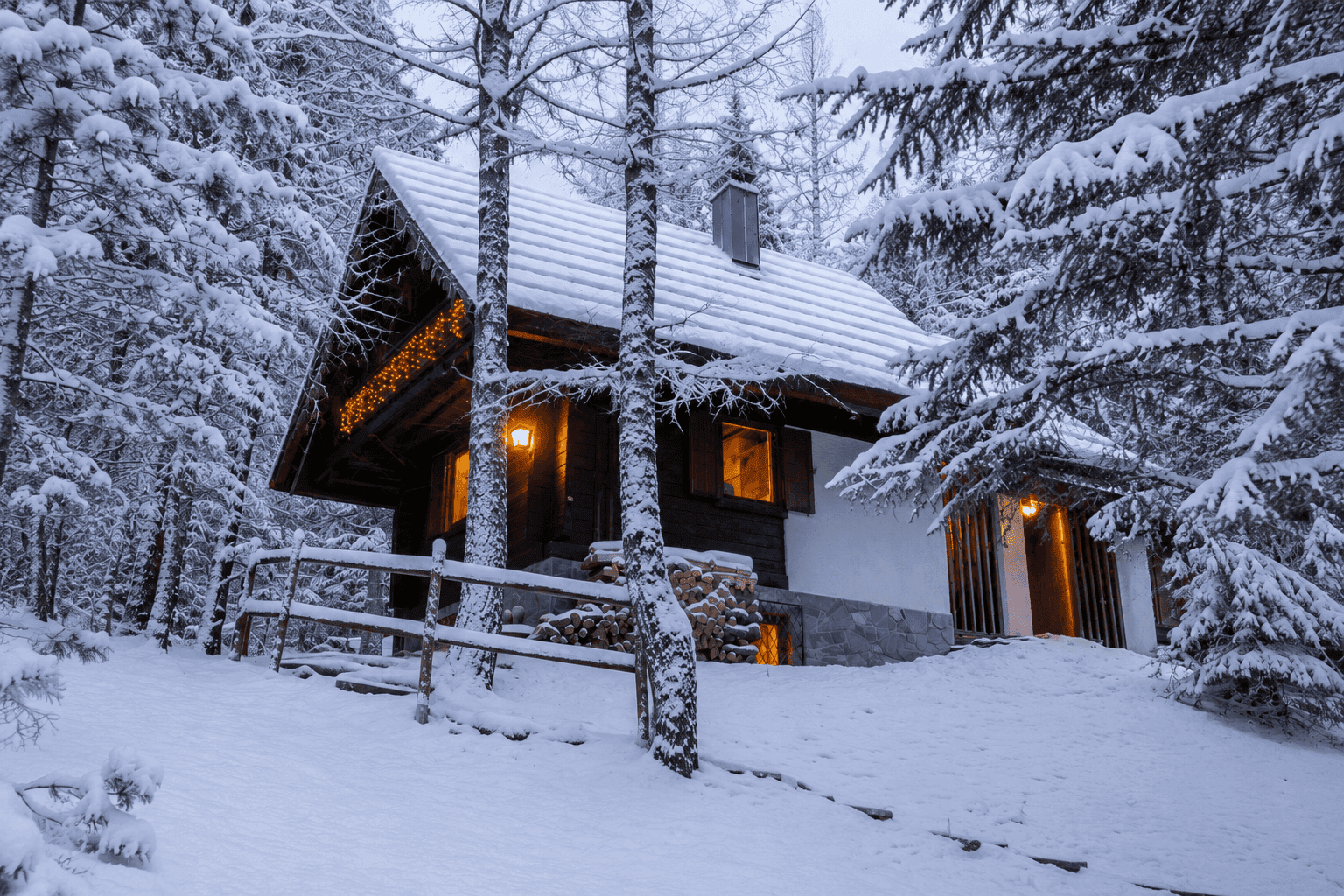 Idyllisches Chalet im Winterwald, umgeben von verschneiten Bäumen und festlicher Beleuchtung.