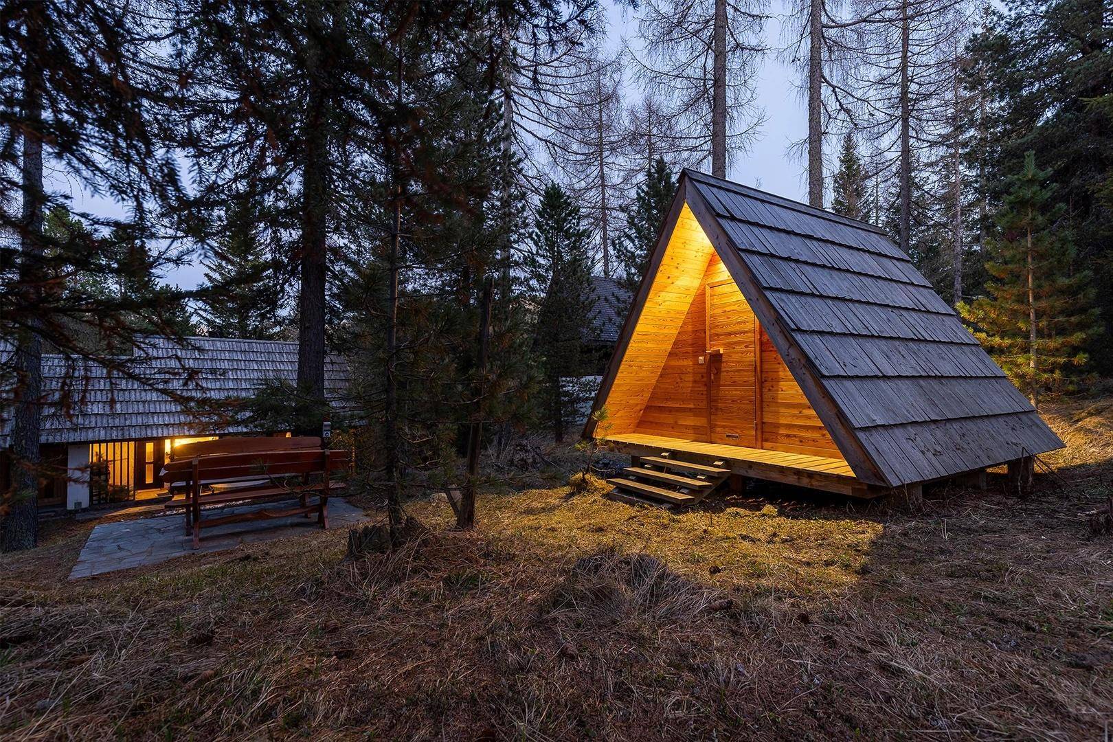 Chalet und beleuchtete A-Rahmen-Struktur in einer Waldlichtung bei Dämmerung.