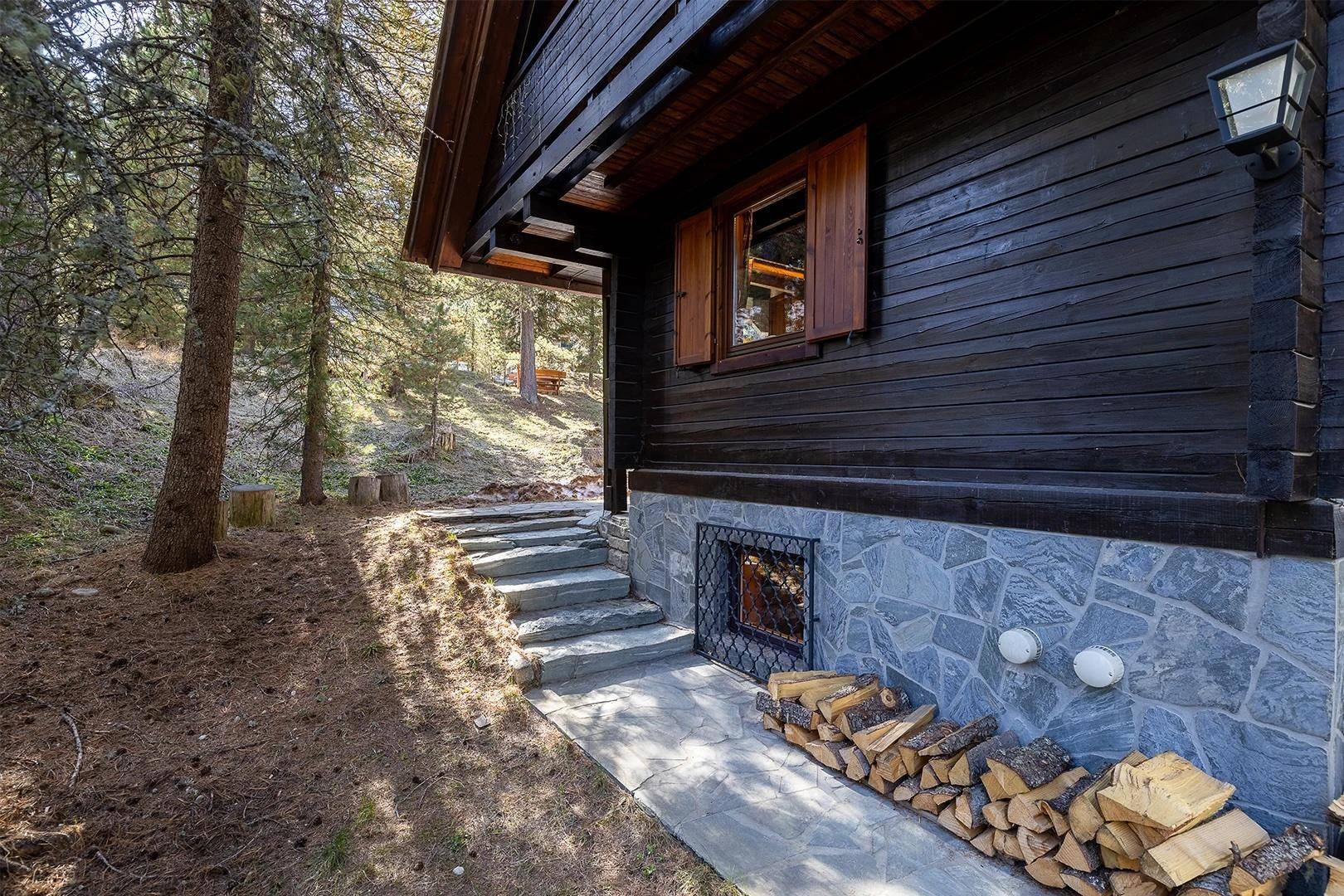 Rustikales Holzhaus mit Steinfundament, umgeben von Bäumen und gestapeltem Brennholz.