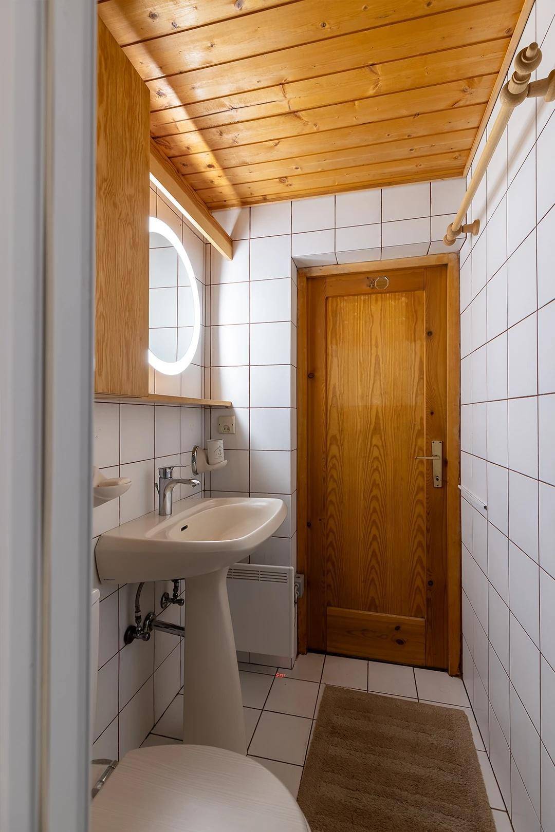 Kleines Badezimmer mit weißen Fliesen, Holzdecke und modernem Waschbecken.