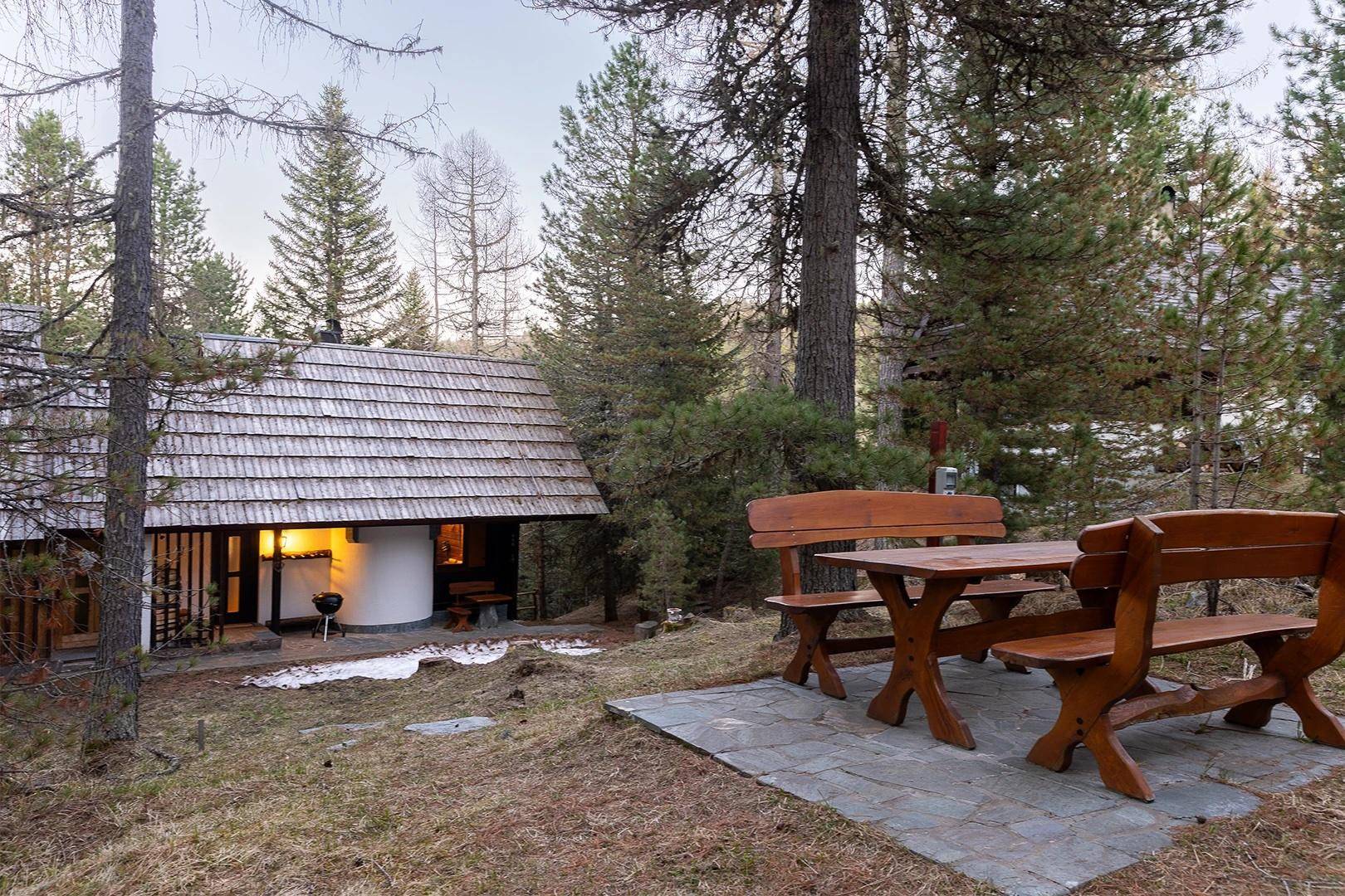 Gemütlicher Außenbereich mit Holztisch und Bänken vor dem Chalet in natürlicher Umgebung.
