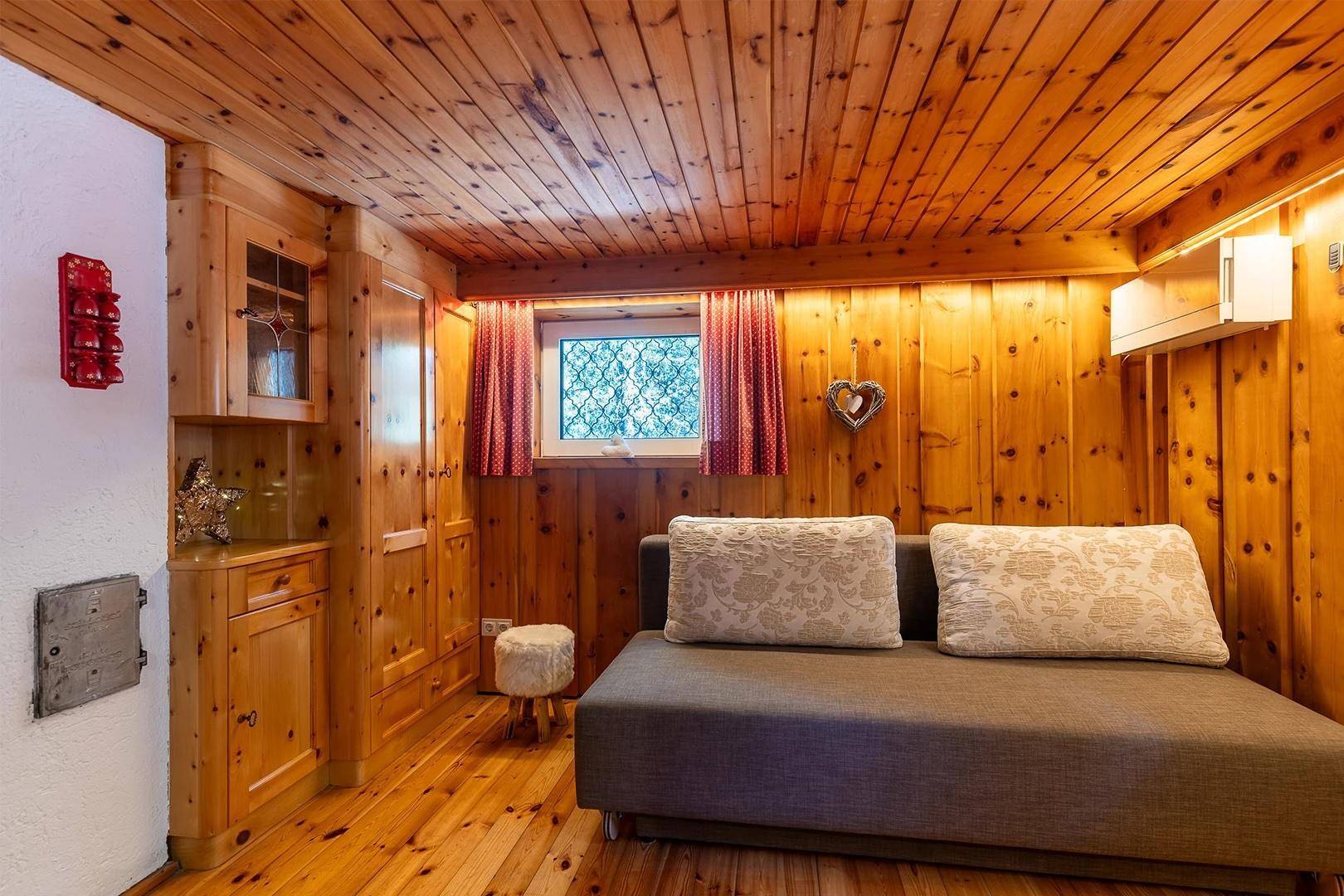 Rustikaler Wohnraum mit Holzwänden, Holzboden und einem bequemen Sofa.