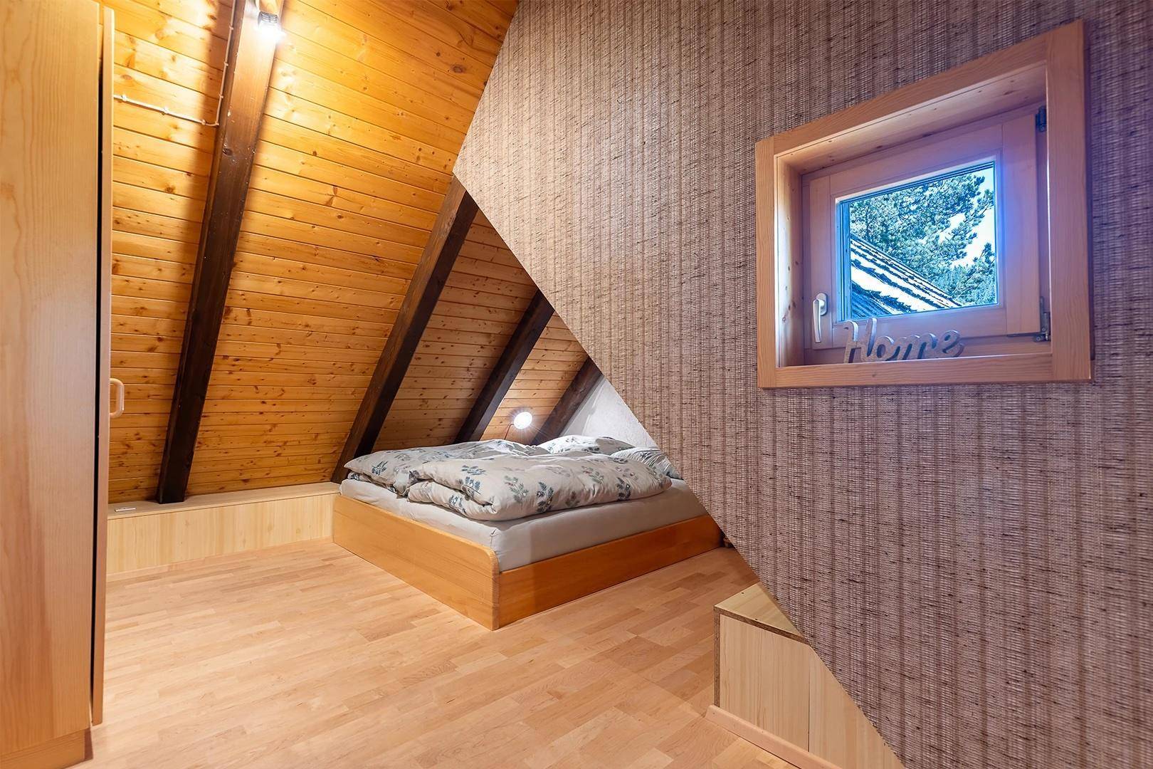 Gemütliches Schlafzimmer im Dachgeschoss mit Holzwänden, Holzbalken und kleinem Fenster.