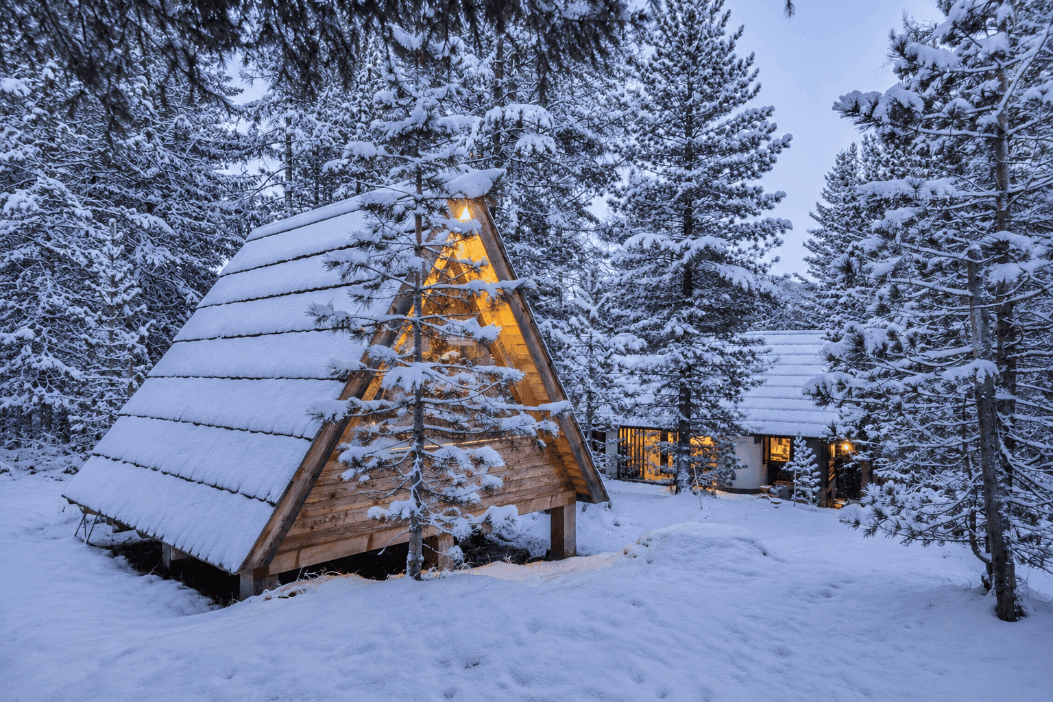 Winterlandschaft mit einem traditionellen Chalet und einer modernen A-Rahmen-Struktur im Schnee.