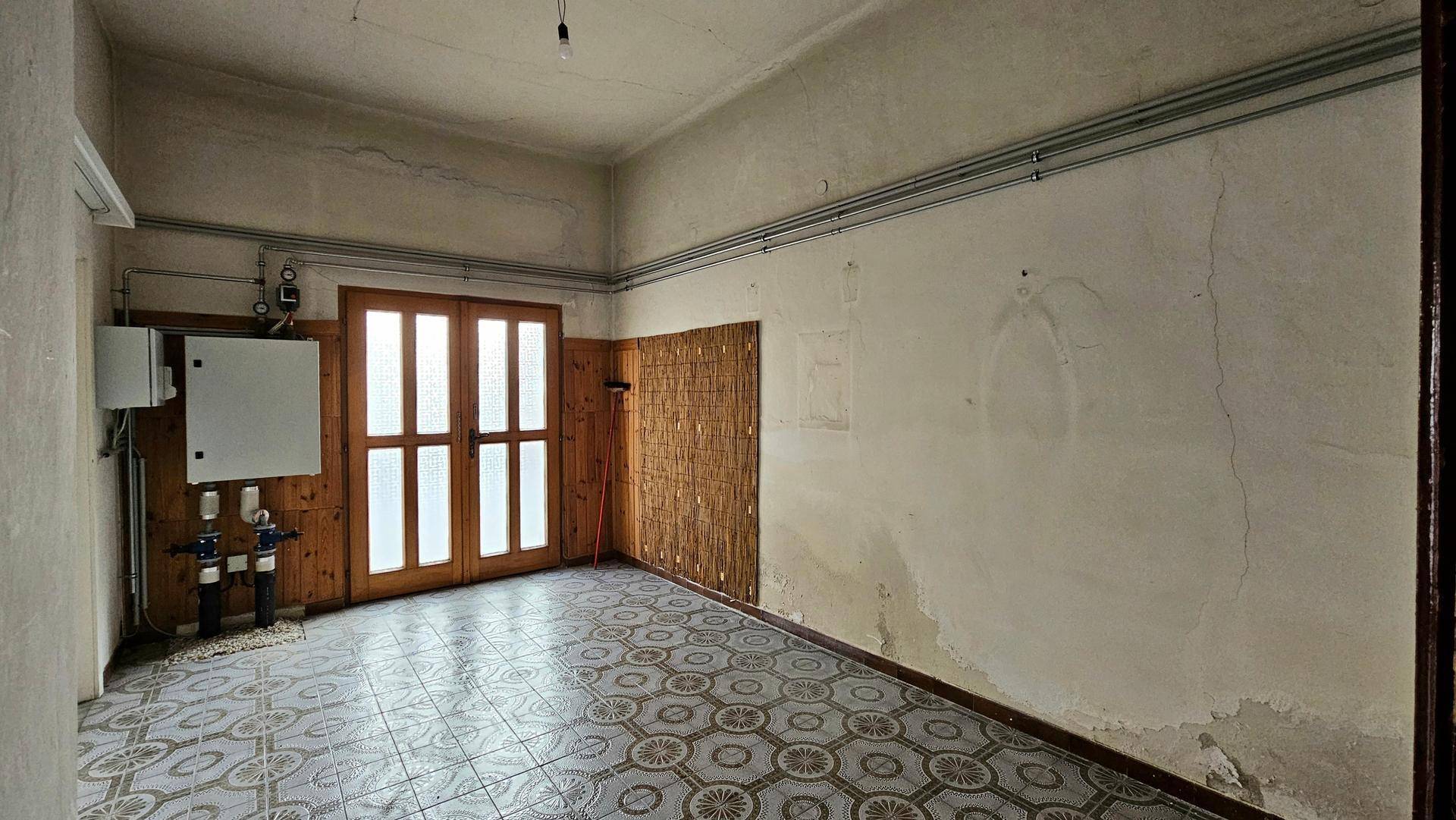 Leerer Raum mit gefliestem Boden, Doppeltür und sichtbaren Installationen an der Wand.