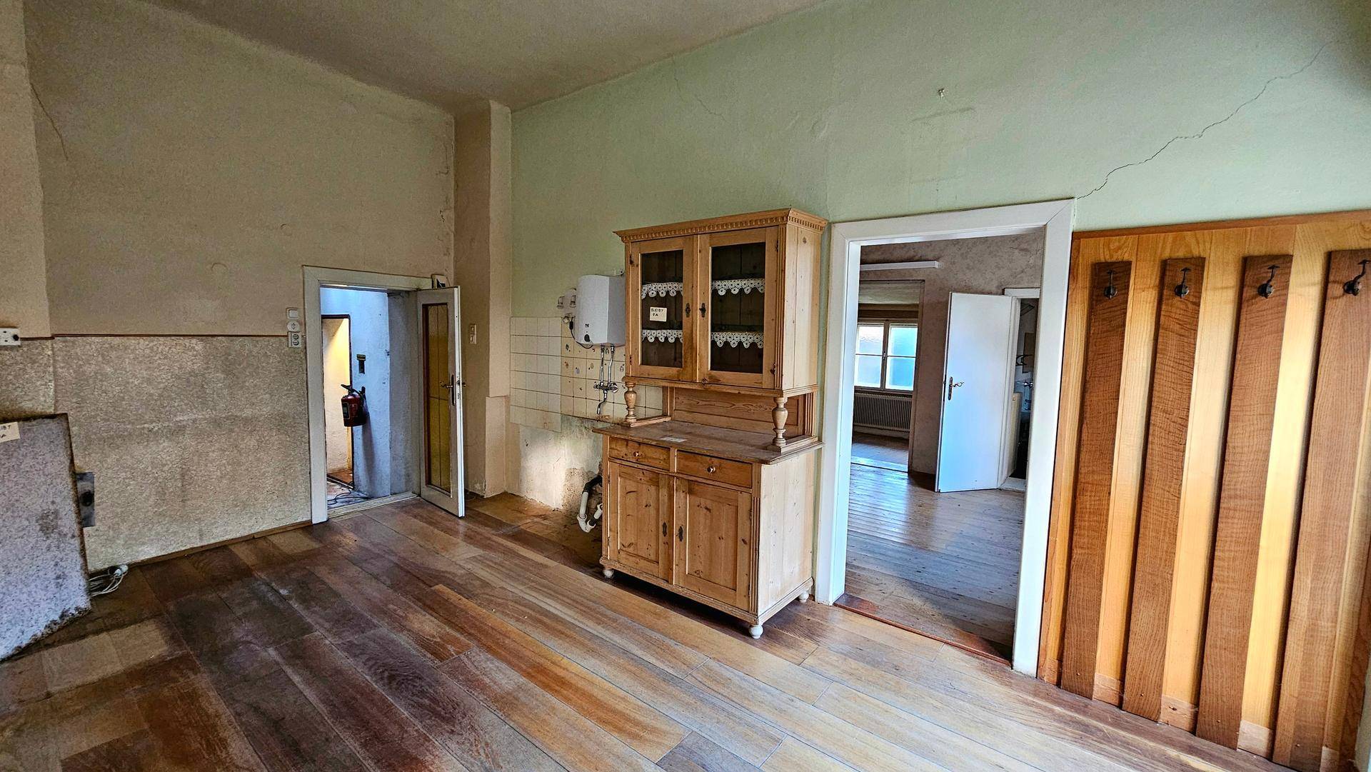 Raum mit Holzdielenboden, einem alten Holzschrank und Zugang zu weiteren Zimmern.