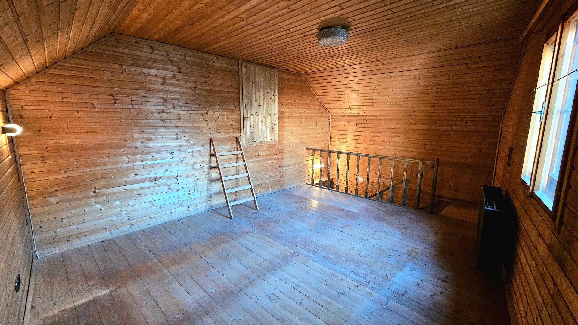 Ausgebauter Dachboden mit Holzverkleidung an Wänden und Decke sowie Holzboden.