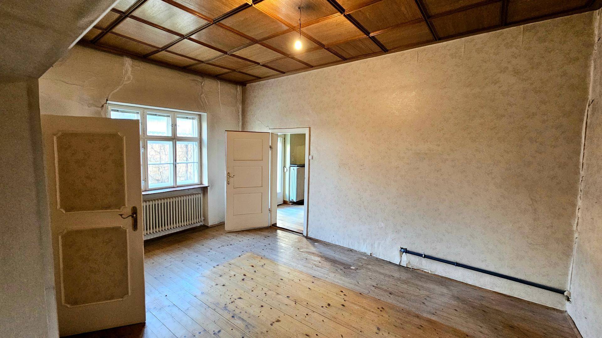 Leerer Raum mit Holzdielenboden, Holzdecke und zwei Fenstern, in renovierungsbedürftigem Zustand.