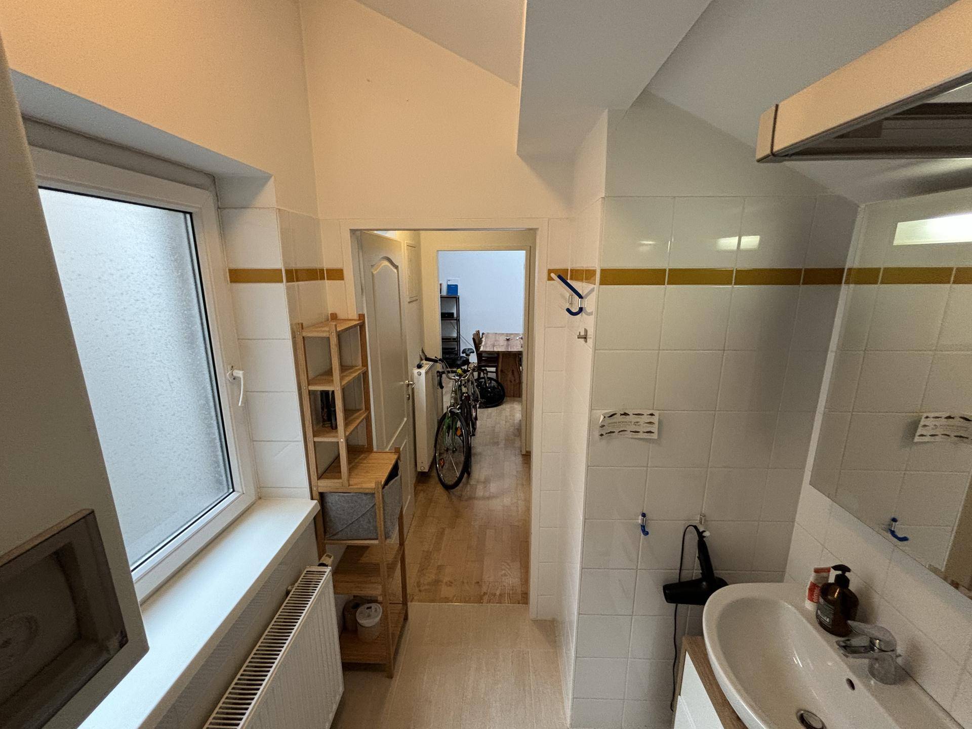 Badezimmer mit Waschbecken und Blick in den Flur, der zu weiteren Räumen führt.
