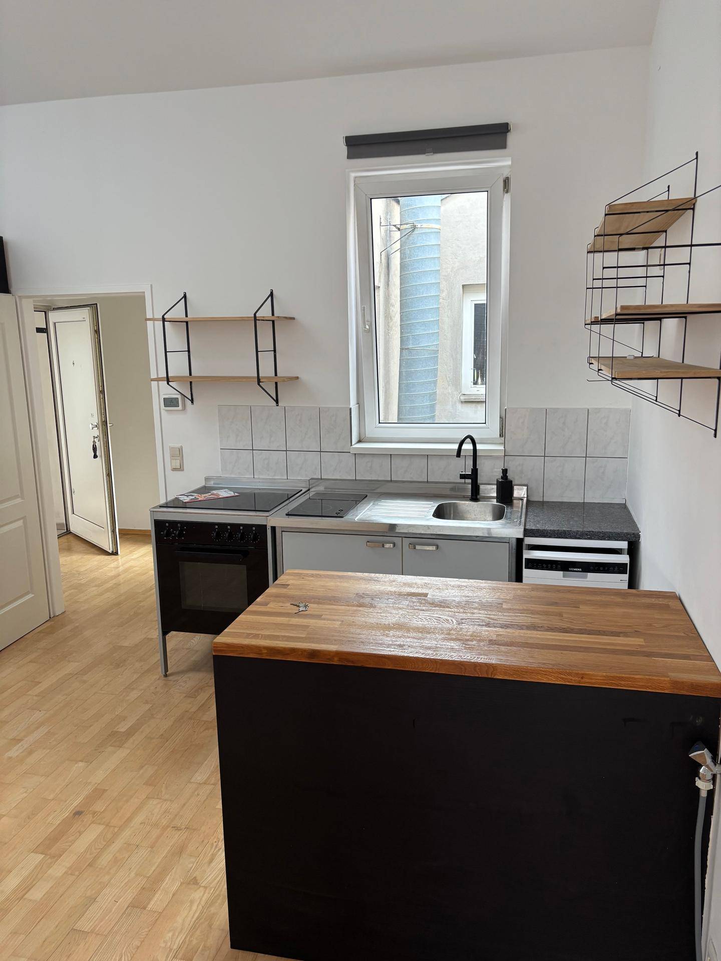 Funktionale Küchenzeile mit Spüle, Herd, Geschirrspüler und Holz-Arbeitsplatte unter einem Fenster.