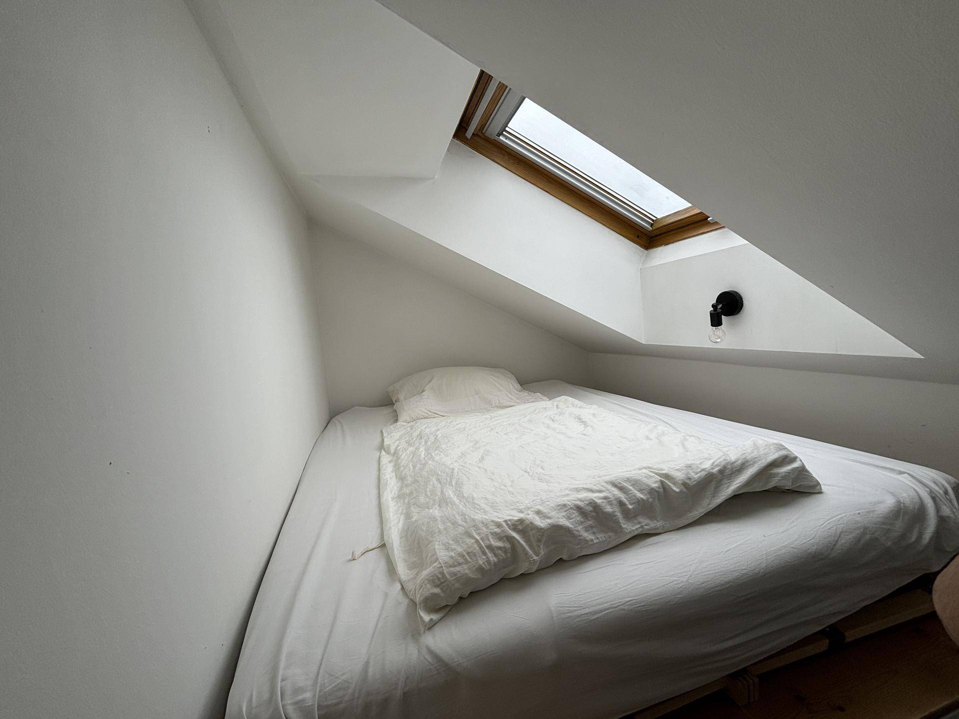 Schlafbereich im Dachgeschoss mit Bett, schräger Decke und einem Dachfenster für natürliches Licht.