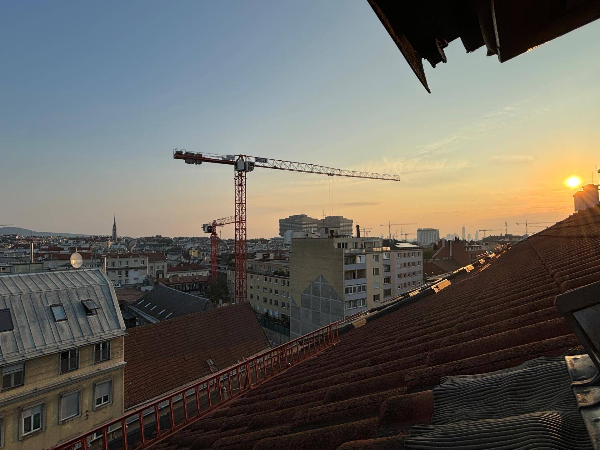 Panoramablick über die Stadt bei Sonnenuntergang, mit Kränen und Dächern im Vordergrund.