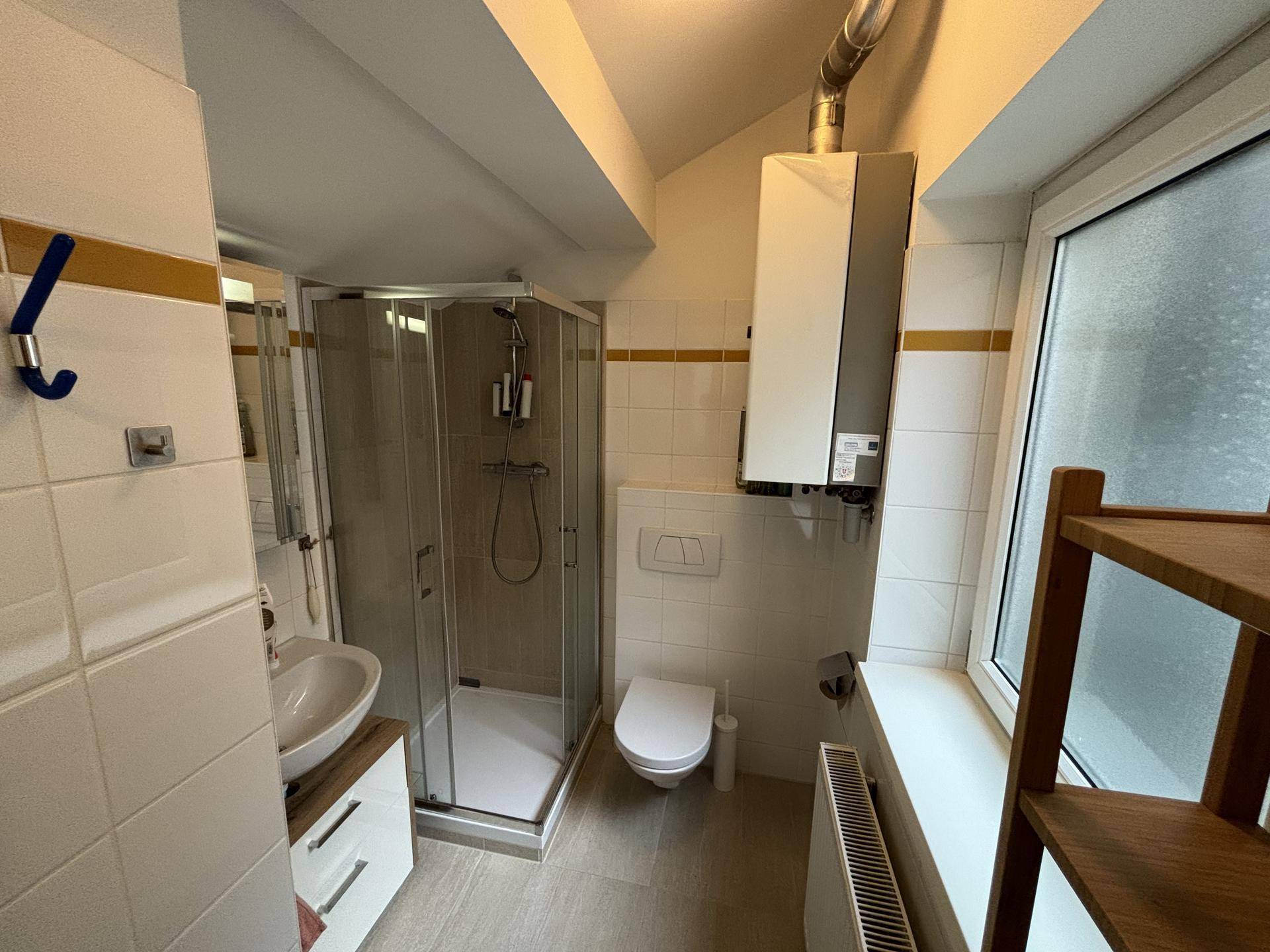 Modernes Badezimmer mit Duschkabine, WC, Waschbecken und Fenster im Dachgeschoss.