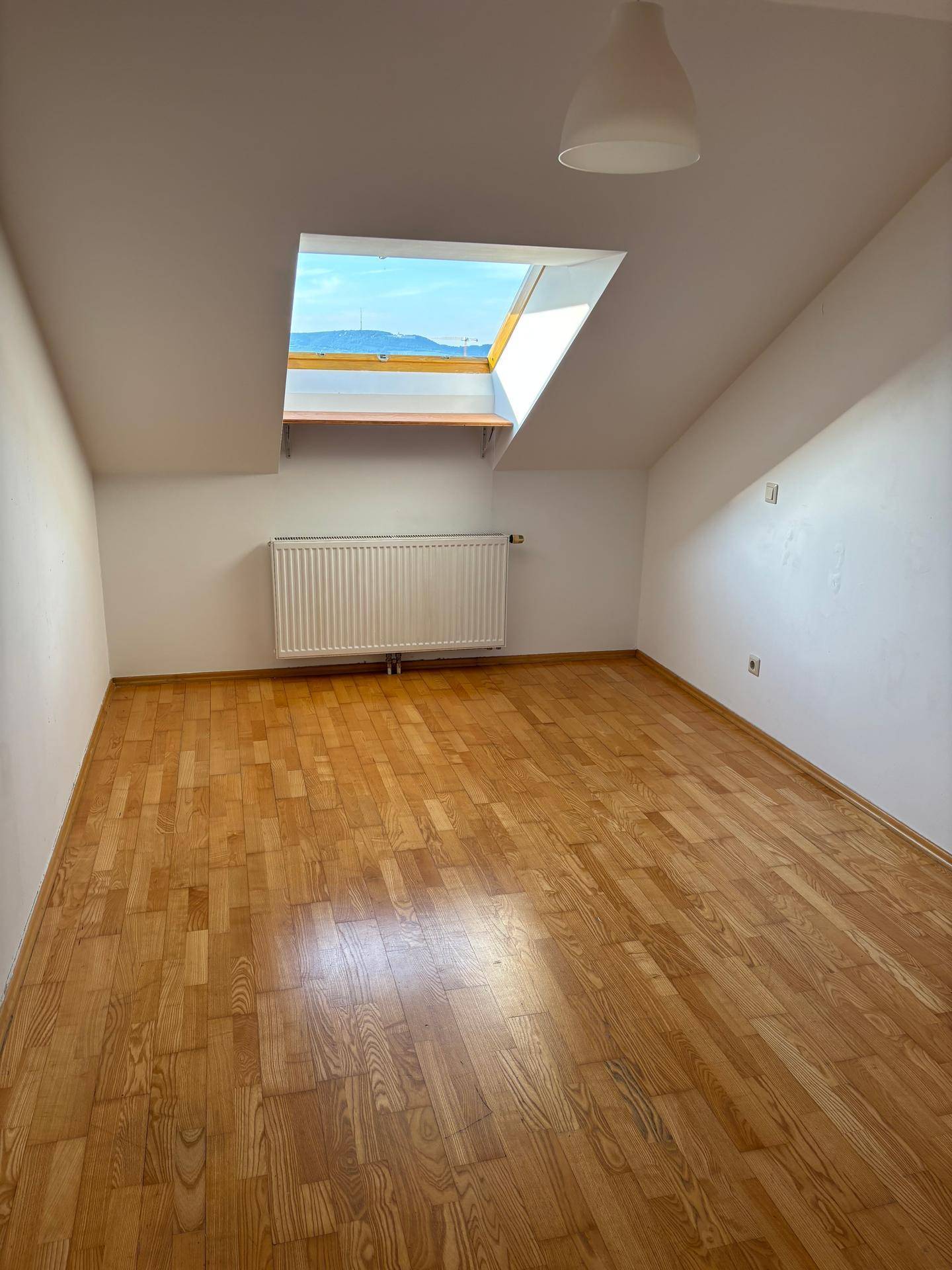 Helles Schlafzimmer im Dachgeschoss mit Holzboden, schrägen Wänden und großem Dachfenster.